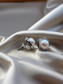 Silberne Ohrstecker mit runder Perle und glitzernder Fassung auf weich gefalteter, champagnerfarbener Seide. Edles und ruhiges Produktfoto.