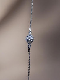 Close-up of a delicate silver bracelet with a round clear stone and fine detailing against a soft neutral background. Minimalist and elegant product photo.