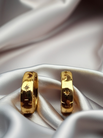 MOKOŠEV Luxusschmuck, goldene Ohrringe mit feinen eingravierten Symbolen auf glänzendem, weißem Satin.