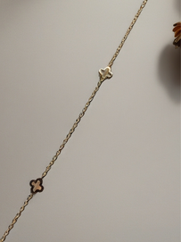 MOKOŠEV Luxusschmuck, feines goldenes Armband mit zwei kleinen Kleeblatt-Elementen auf neutralem Hintergrund.