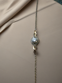 MOKOŠEV Luxusschmuck, zartes goldenes Armband mit funkelndem Kristallanhänger auf elegant drapiertem Stoff.