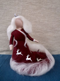 Weihnachtsfee in dunkelrotem Kleid mit Schleppe und weißen Verzierungen. Eine weiße Schleppe fließt von den Schultern in den Saum wie Schnee. Silberne Rentiere schmücken das Kleid und eines den Kopf als Krone auf den langen, weißen Haaren.