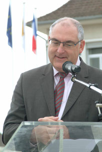 élu maire devant un micro et pupitre devant mairie et drapeaux français et européen en extérieur sourire et mains jointes