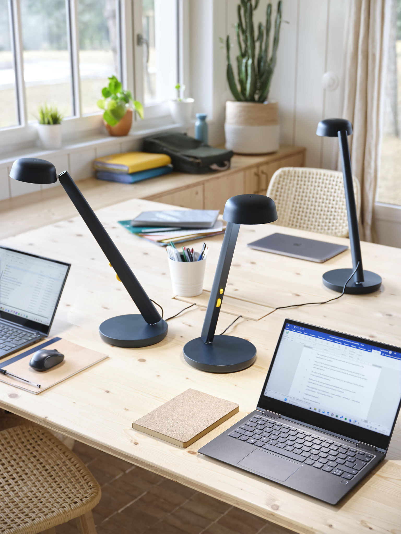 Espace de coworking lumineux avec table en bois clair, ordinateurs portables, carnets et lampes de bureau au design moderne bleu nuit.