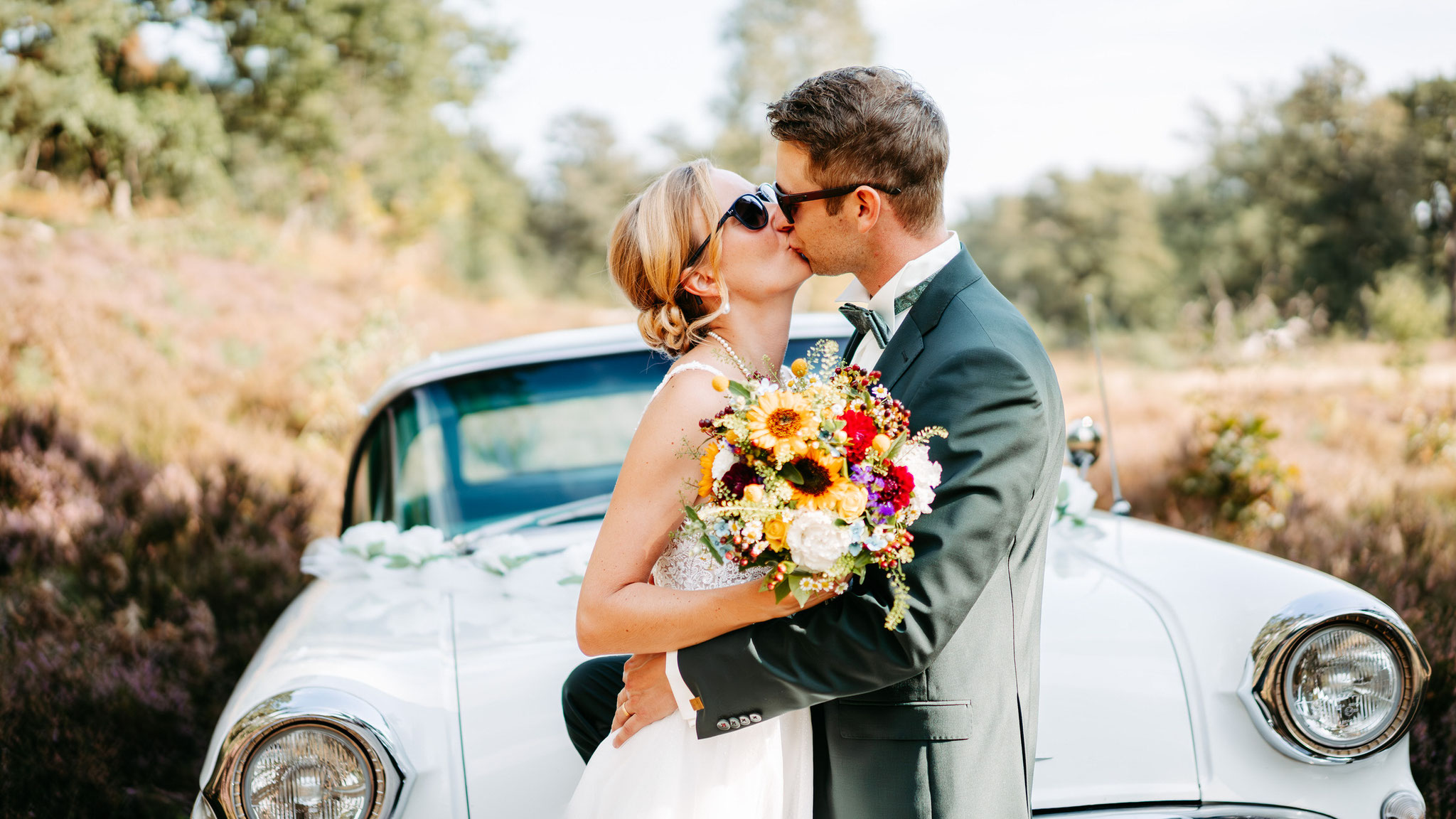 Hochzeitspaar mit Hochzeitsauto in der Göhrder Heide