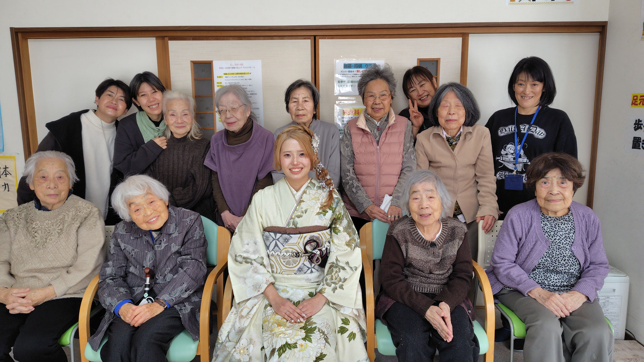 成人式の晴れ着姿の女性を囲むご利用者と職員の集合写真