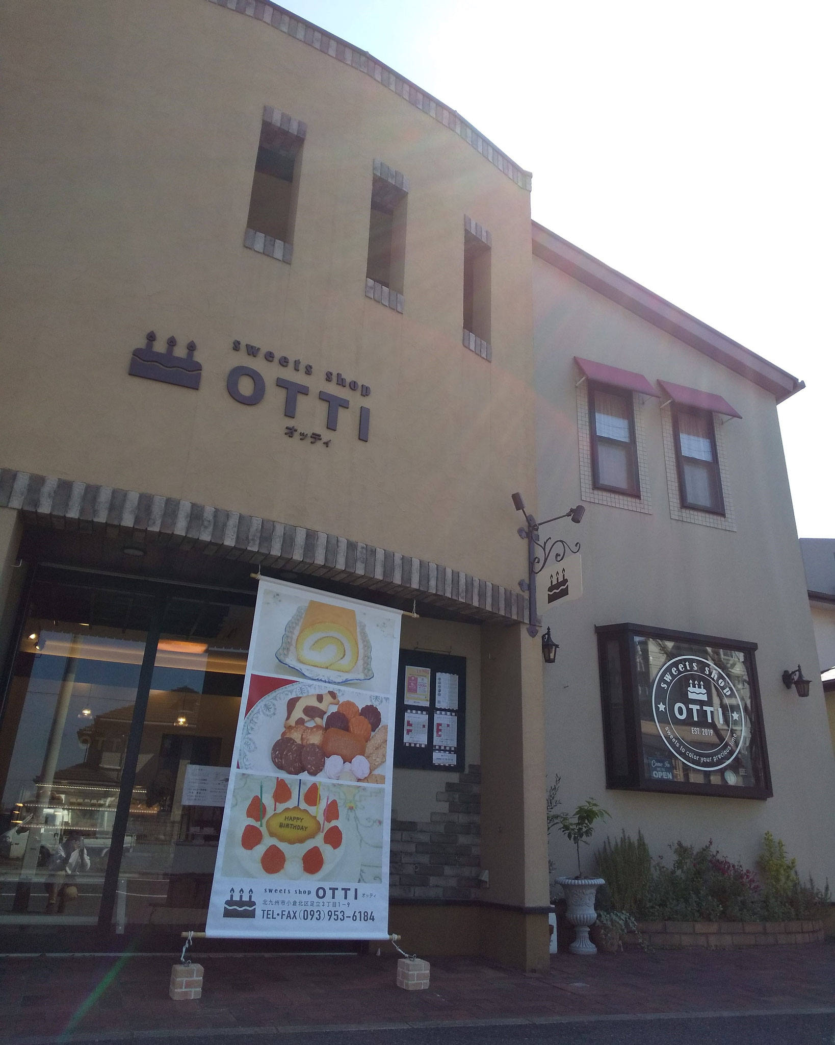店舗外観です。大きなタペストリーやOTTIサイン、ケーキの看板が目印です。