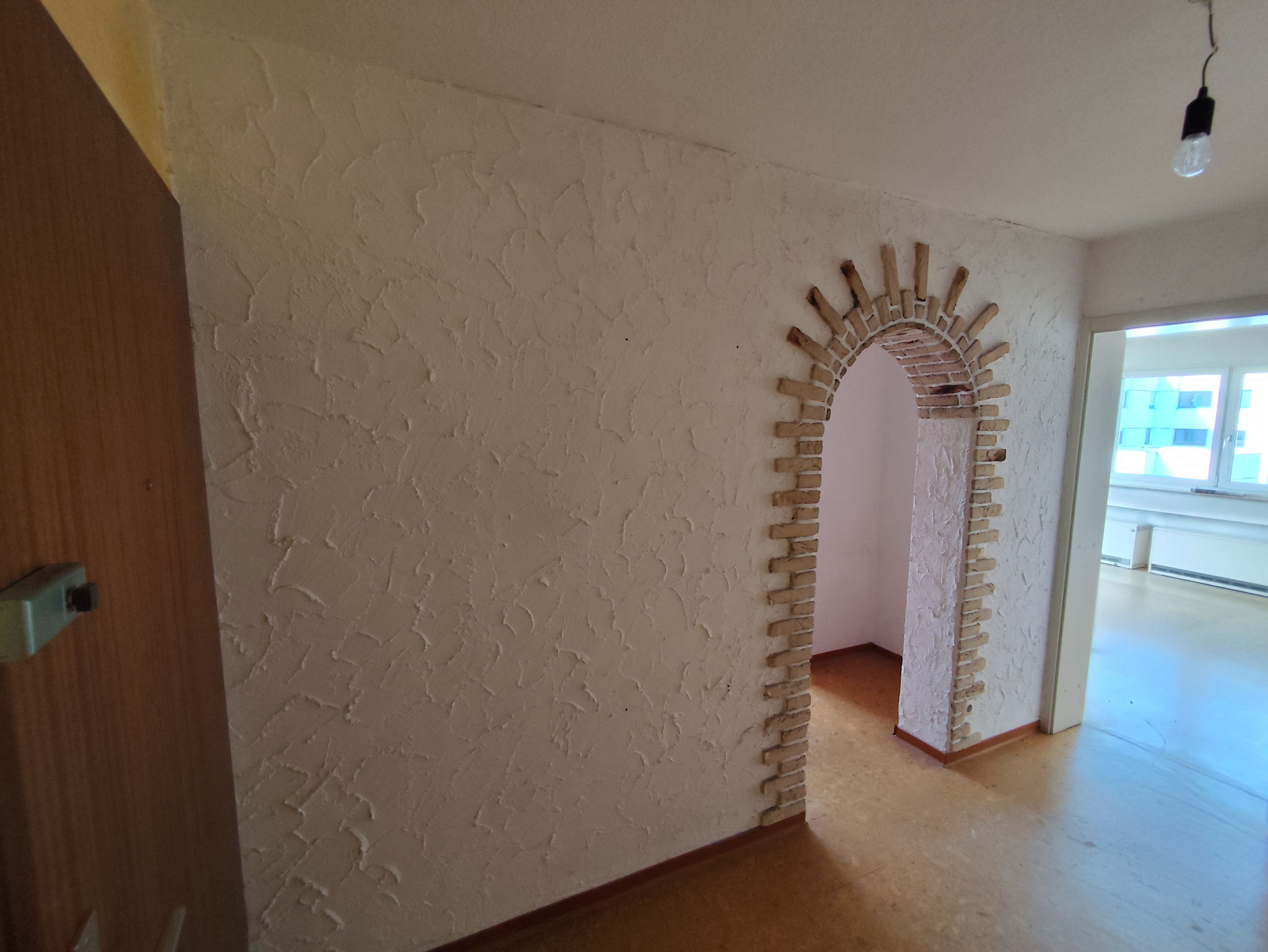 Wand mit sehr groben Putz und Rundbogen.