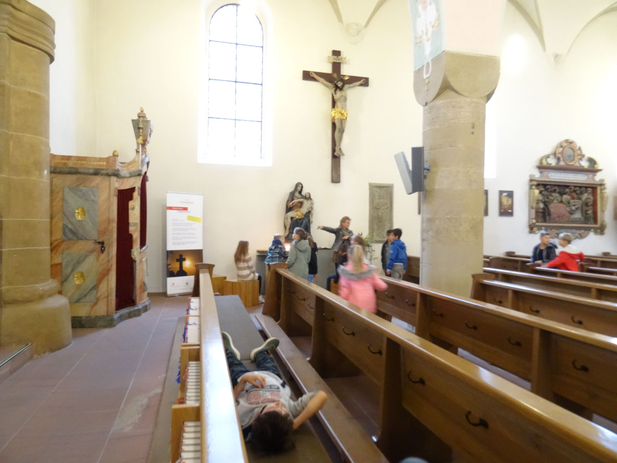 Die Kinder schauen sich die Decke der Kirche an und liegen dabei auf den Bänken