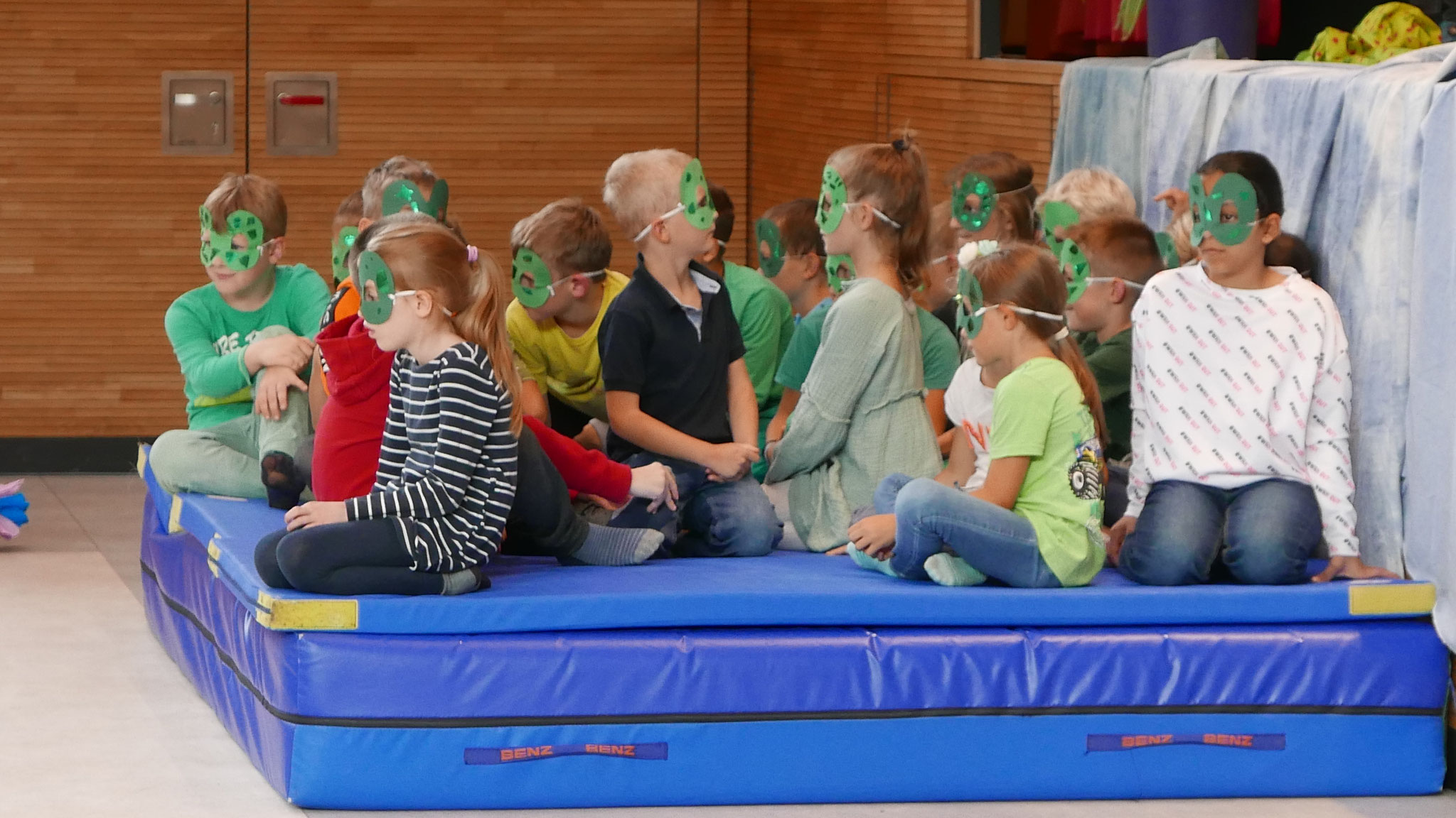 Kinder, als Frösche verkleidet, sitzen im Teich, also auf einer blauen Matte