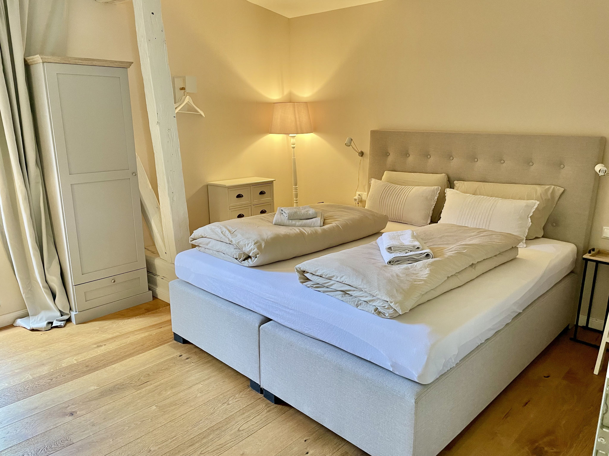 Vom Wohnzimmer gelangt ihr in das Schlafzimmer. Hier wartet ein 1,80m breites Boxspringbett auf euch. Dafür haben wir zwei mobile XXL-Rausfallschutze. 