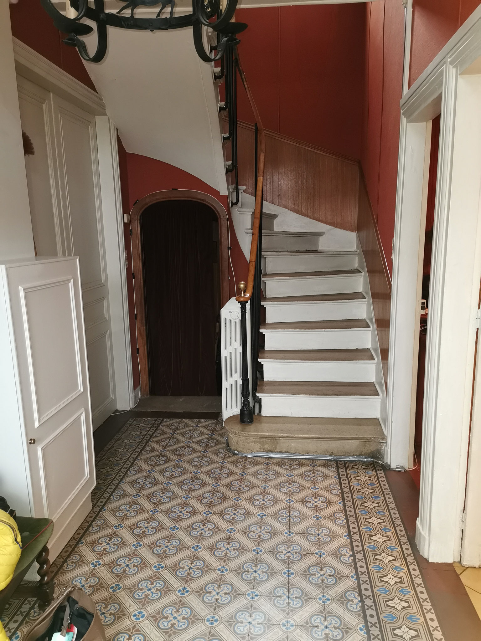 Entrée sombre avant rénovation, avec papier peint rouge, dans une maison de maître située dans l’Oise.