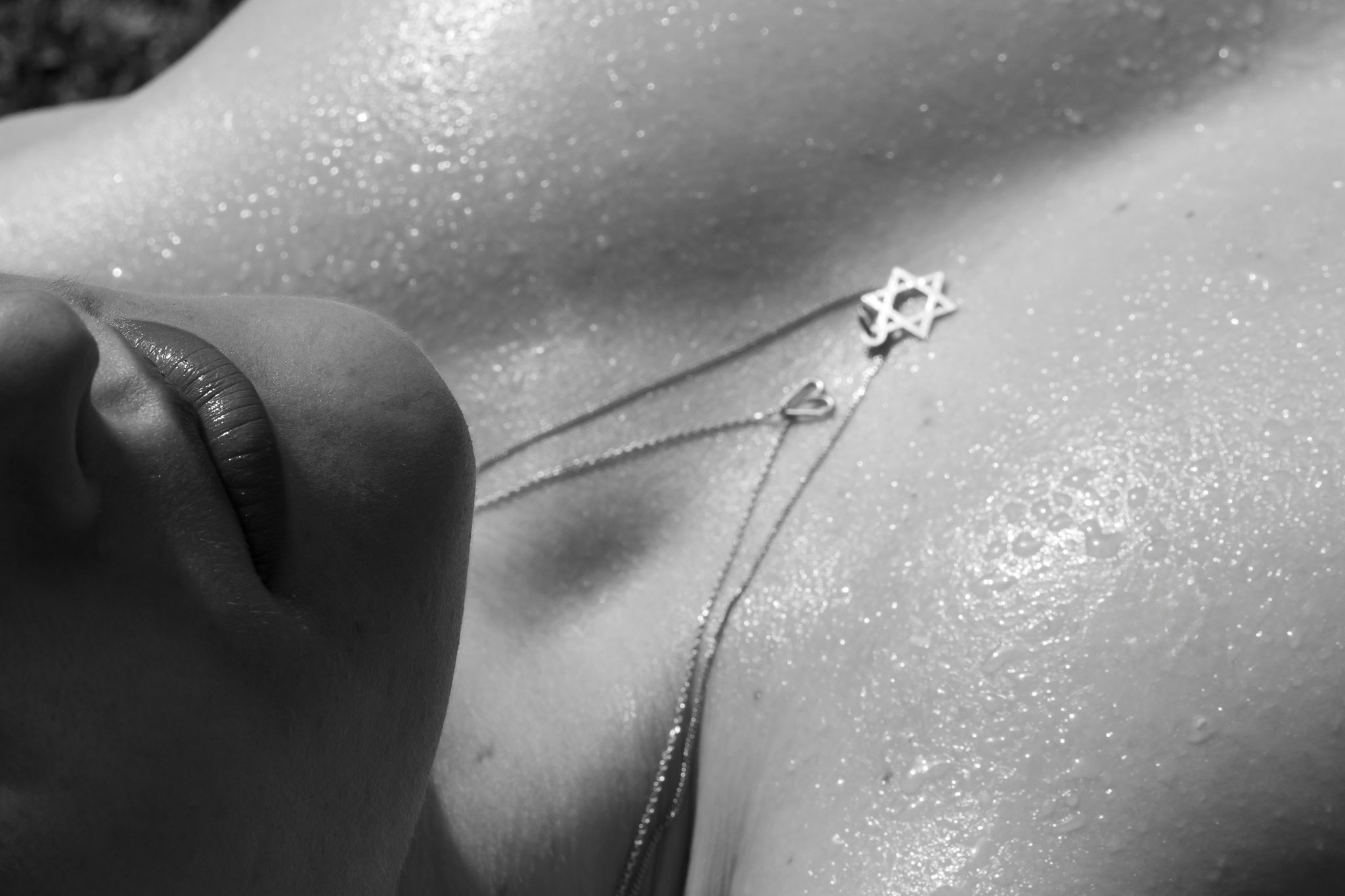 Sinnliche Schwarz-Weiß-Nahaufnahme eines weiblichen Dekolletés mit Wassertropfen und feiner Kette, bei der die Lippen im Vordergrund liegen