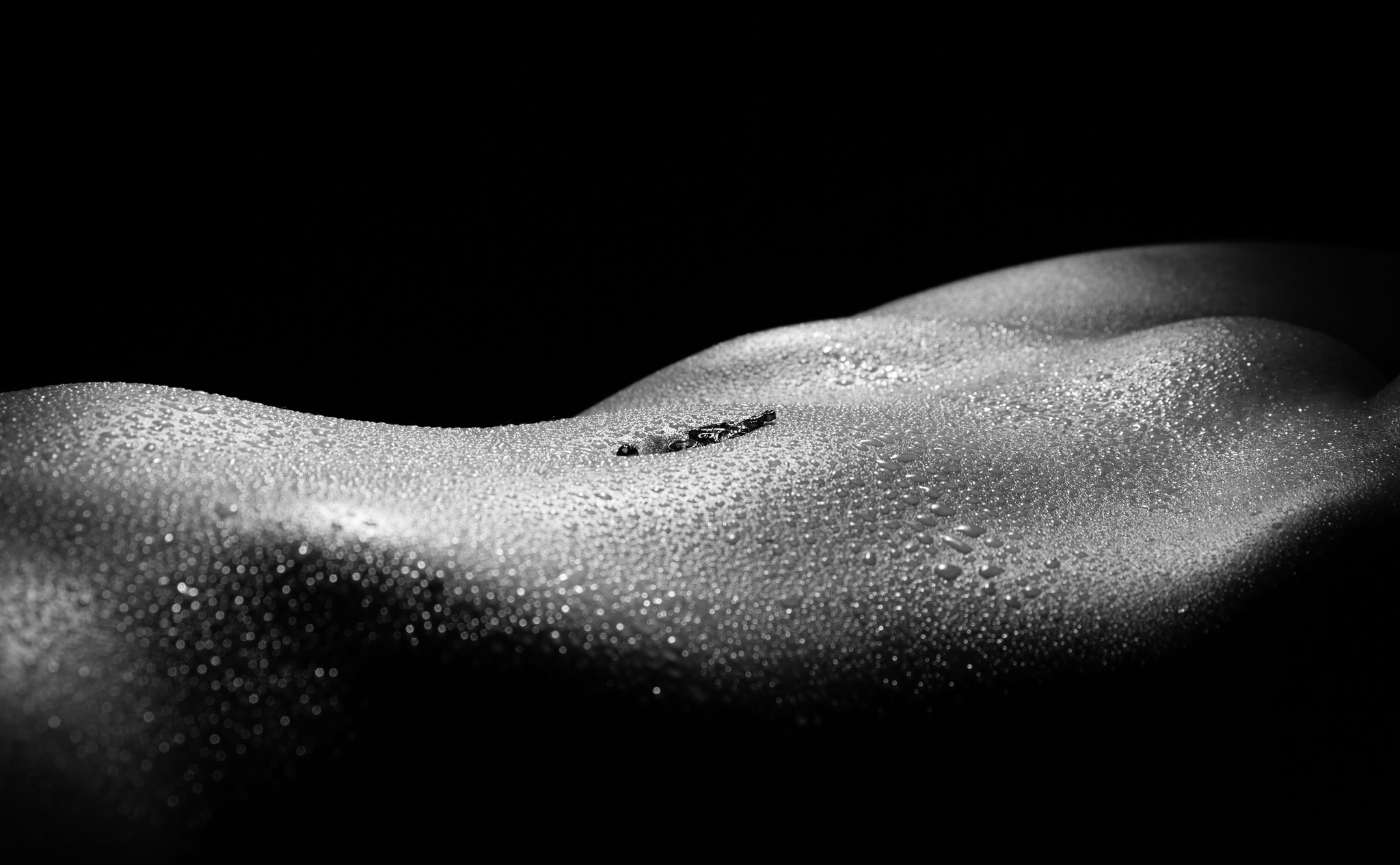 Künstlerisches Schwarz-Weiß-Studiofoto eines weiblichen Bauches mit Wassertropfen im dramatischen Licht