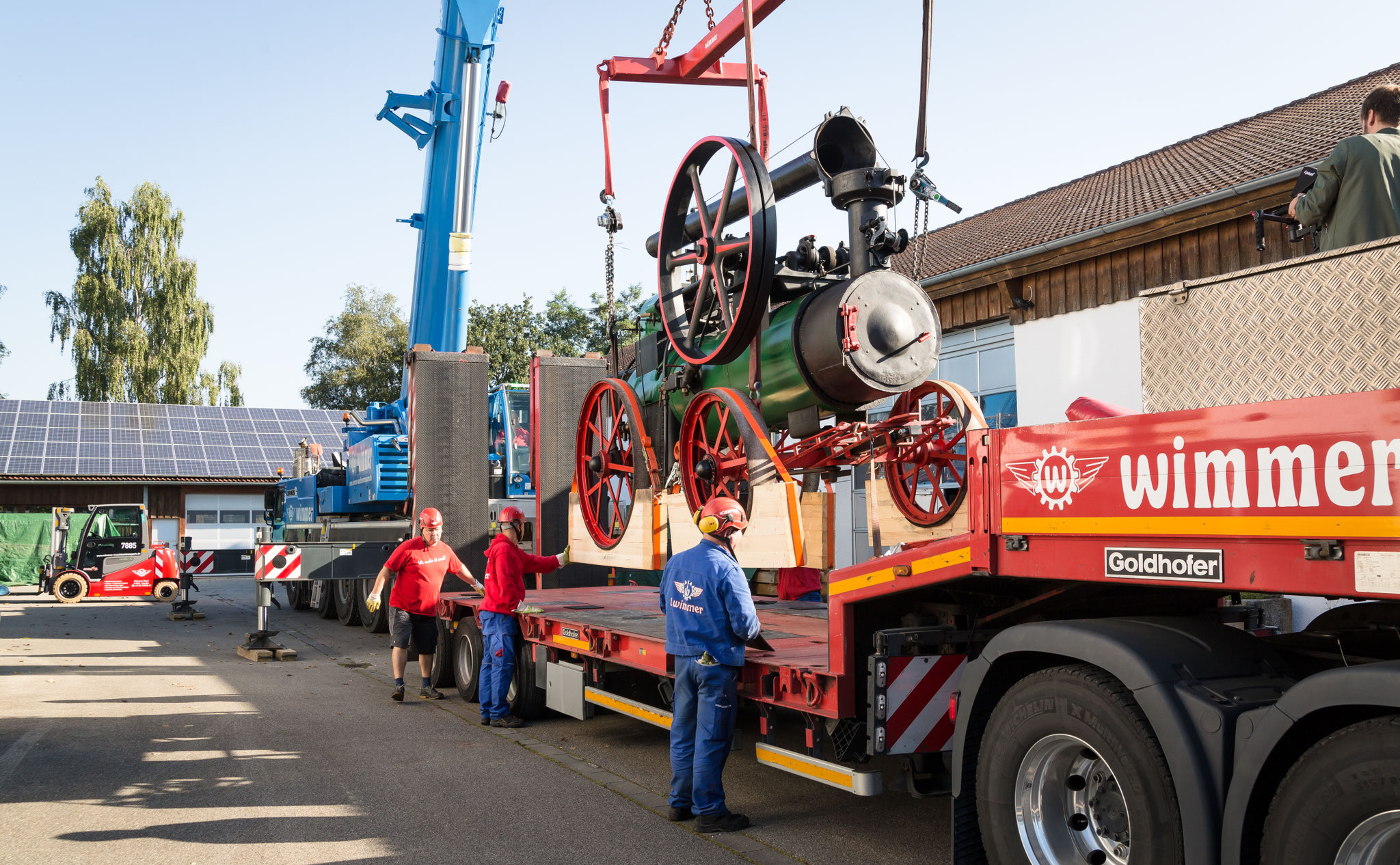 Werbefoto eines Schwertransports: historische Dampfmaschine wird per Kran auf einen Wimmer-LKW verladen – industrielle Werbefotografie für Spedition und Spezialtransporte