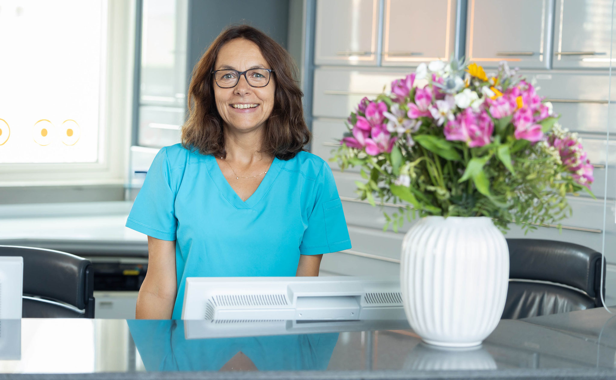 Blumen am Empfang einer Zahnarztpraxis mit Mitarbeiterin