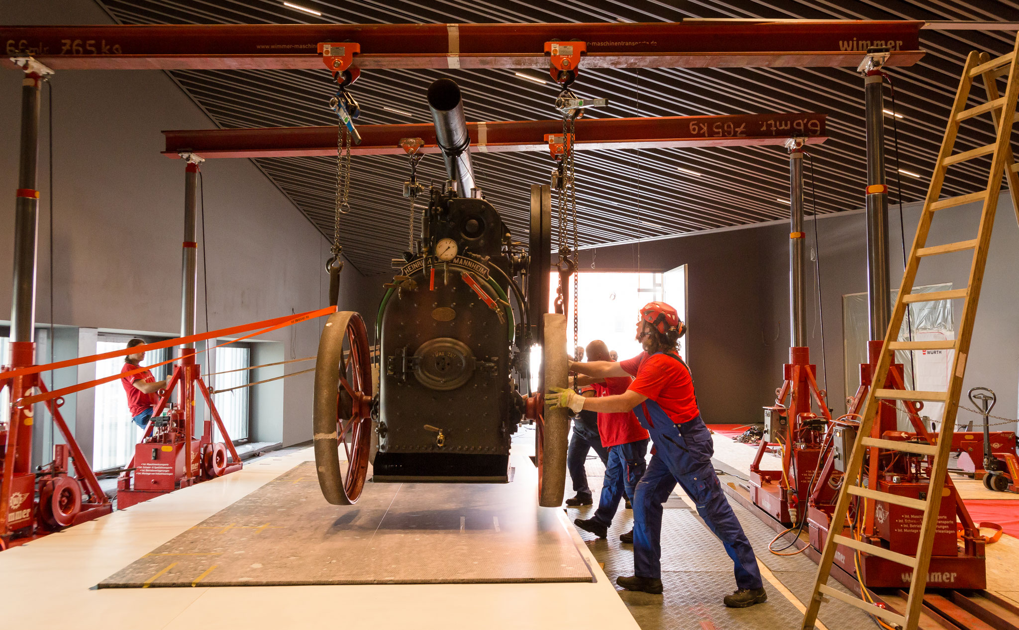 Industriefotografie: Mitarbeiter bewegen eine schwere Maschine mit Hallenkran – professionelles Werbefoto für Industriebetrieb und Maschinenbau