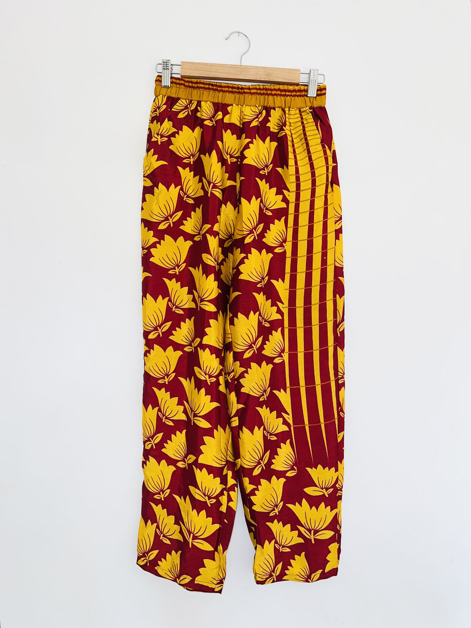 Pantalon bordeaux en sari recyclé suspendu sur cintre, vue complète de loin, motifs jaunes indiens visibles.