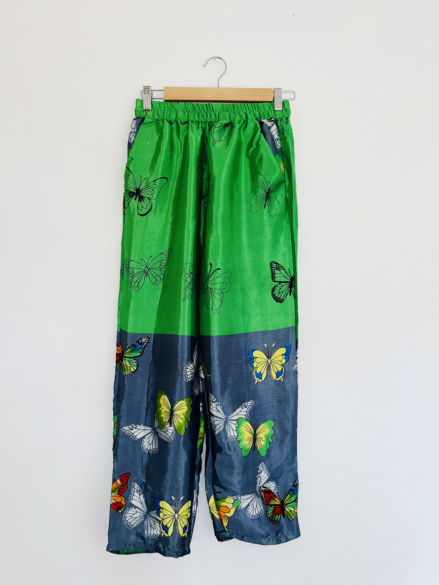Pantalon vert vif et gris souris en sari recyclé avec papillons noirs et colorés suspendu sur cintre, vue complète