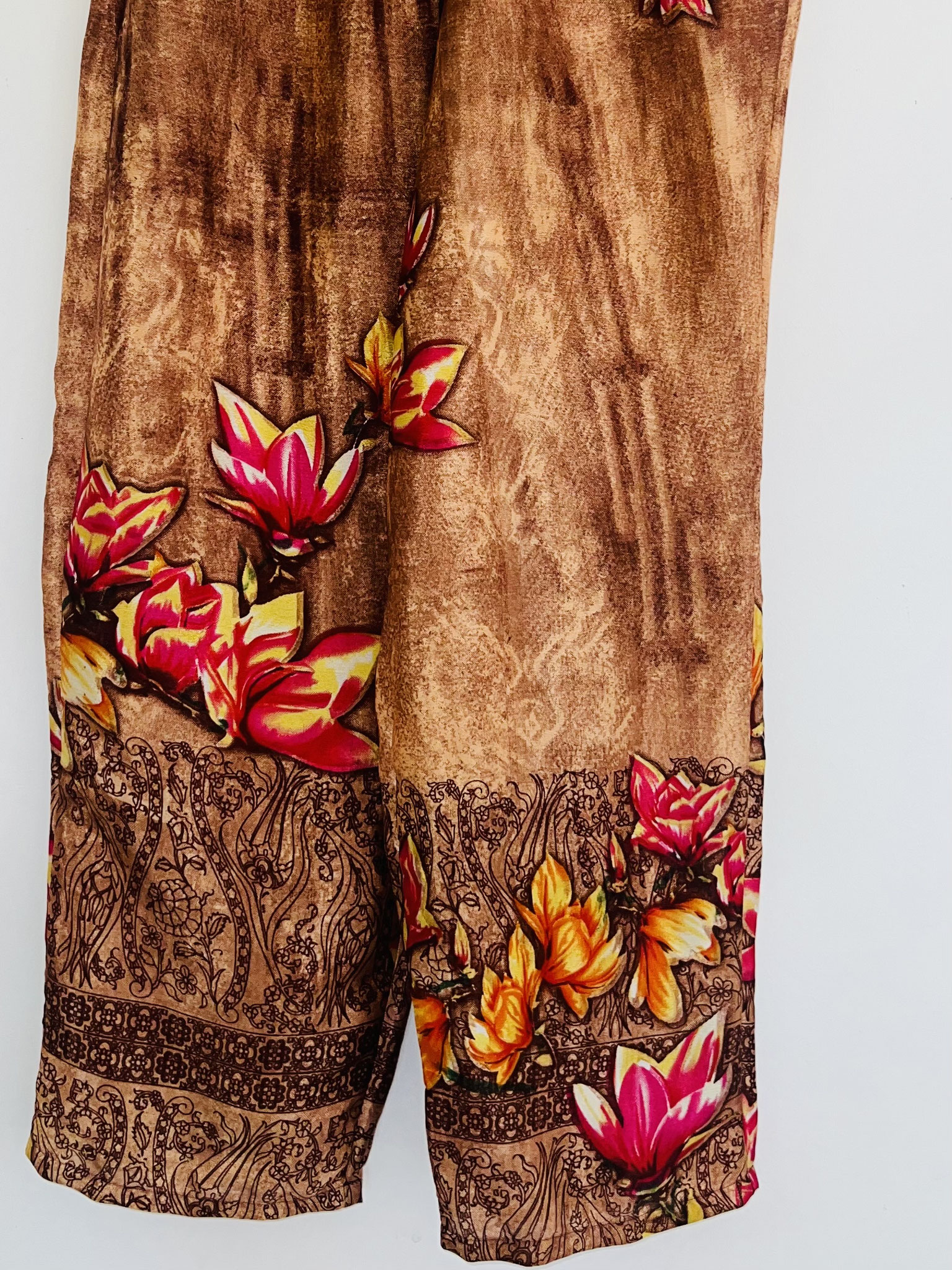 Gros plan sur le bas du pantalon marron et beige en sari recyclé avec fleurs jaunes et roses et inscriptions indiennes suspendu sur cintre