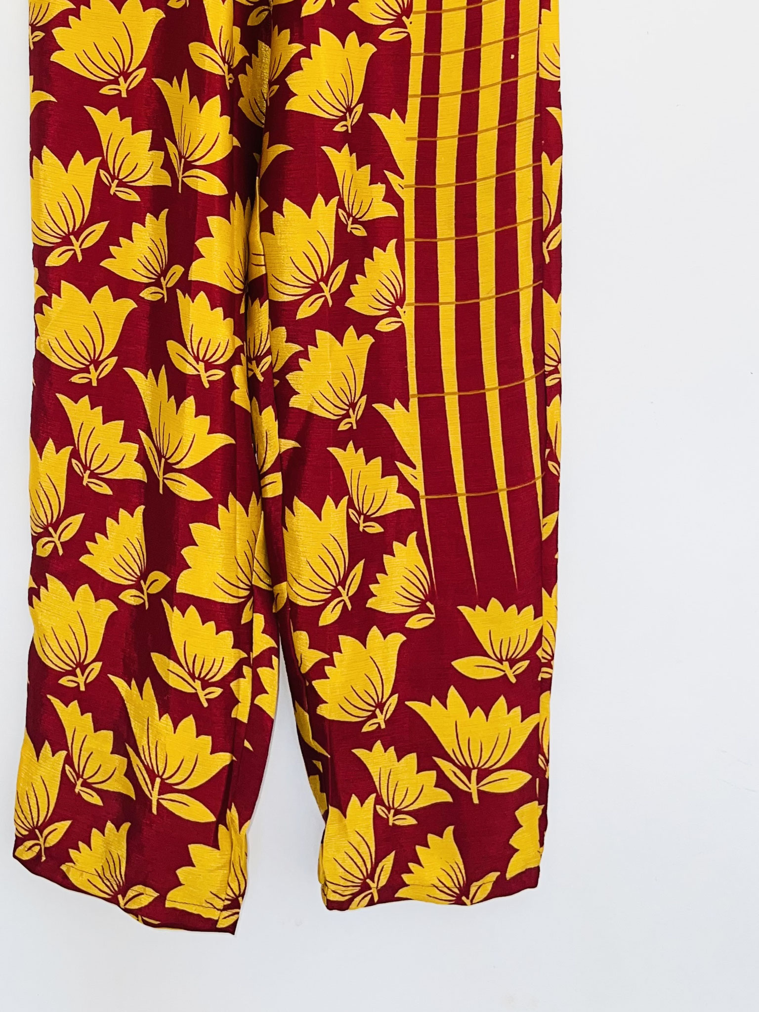  Gros plan sur le bas du pantalon bordeaux en sari recyclé, motifs jaunes asymétriques sur la jambe, suspendu sur cintre.