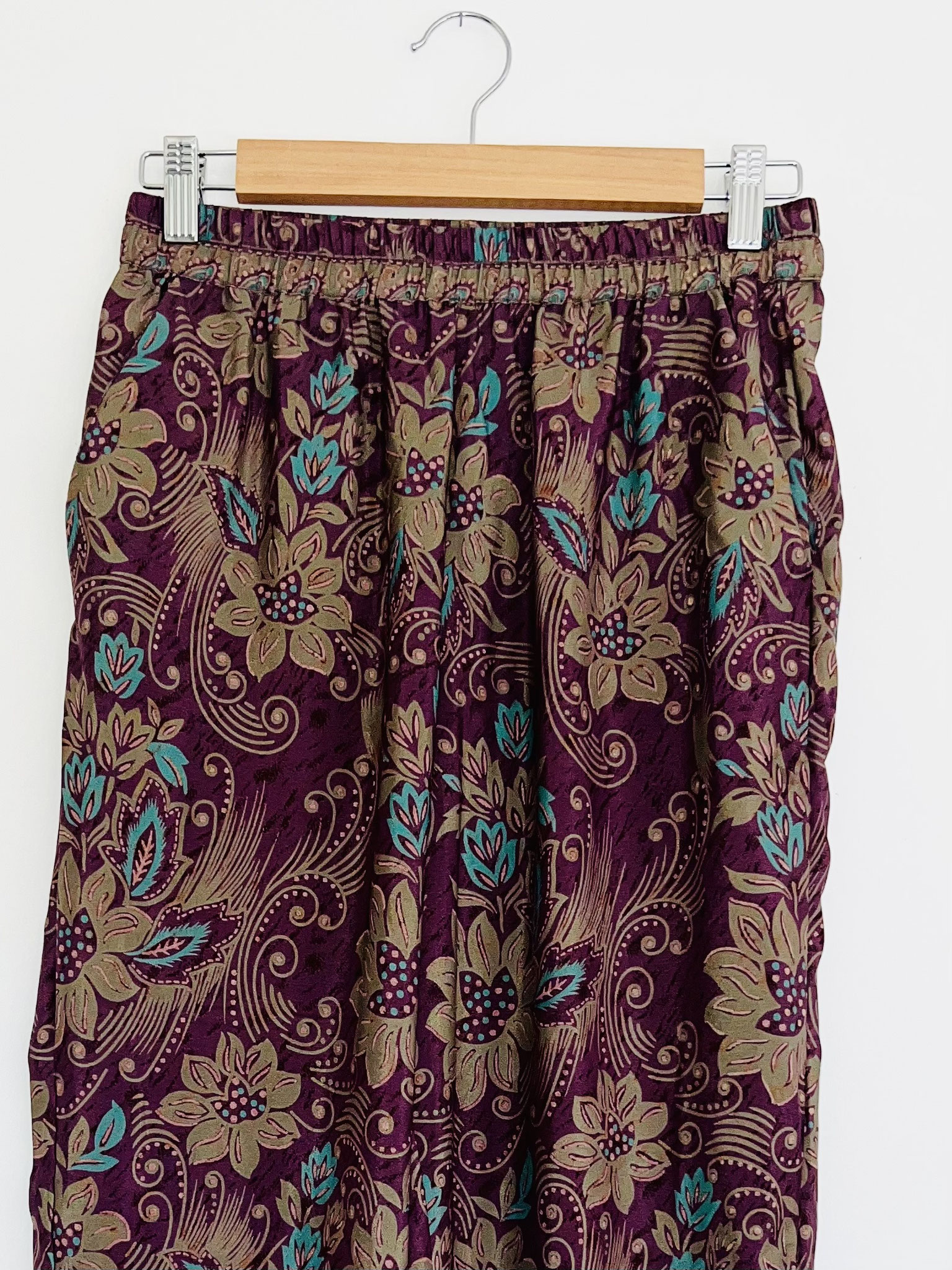  Gros plan sur la partie haute du pantalon violet en sari recyclé suspendu sur cintre, motifs indiens et grosses fleurs vert turquoise
