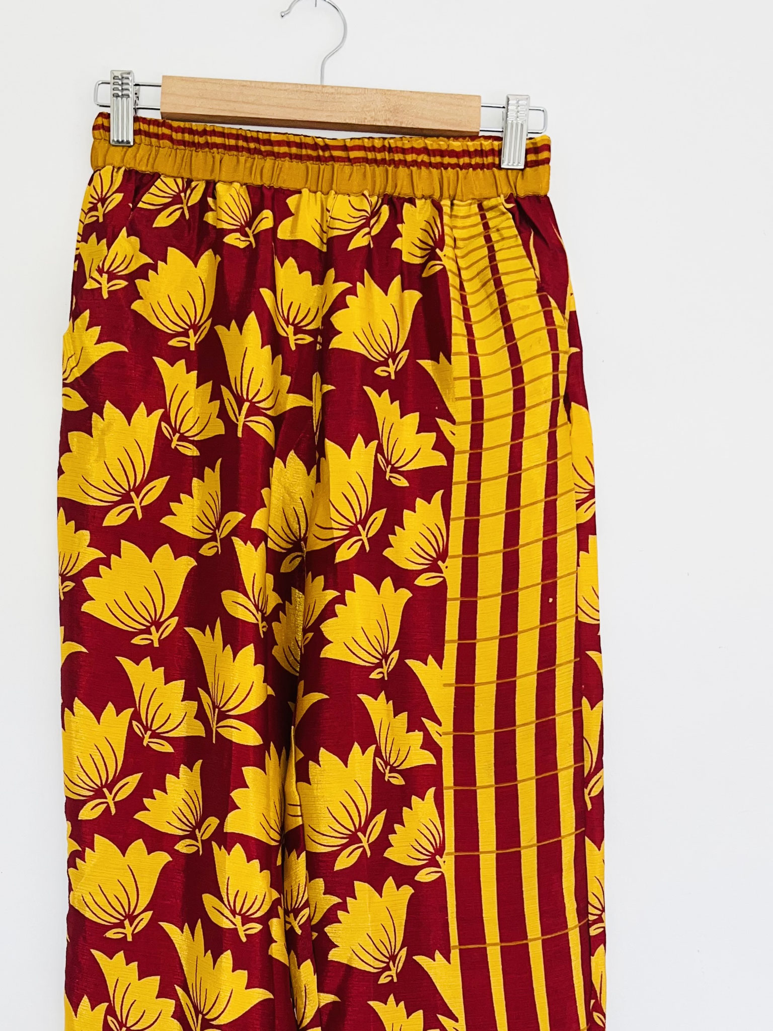  Gros plan sur la partie haute du pantalon bordeaux en sari recyclé suspendu sur cintre, motifs jaunes symétriques et ceinture bordeaux.