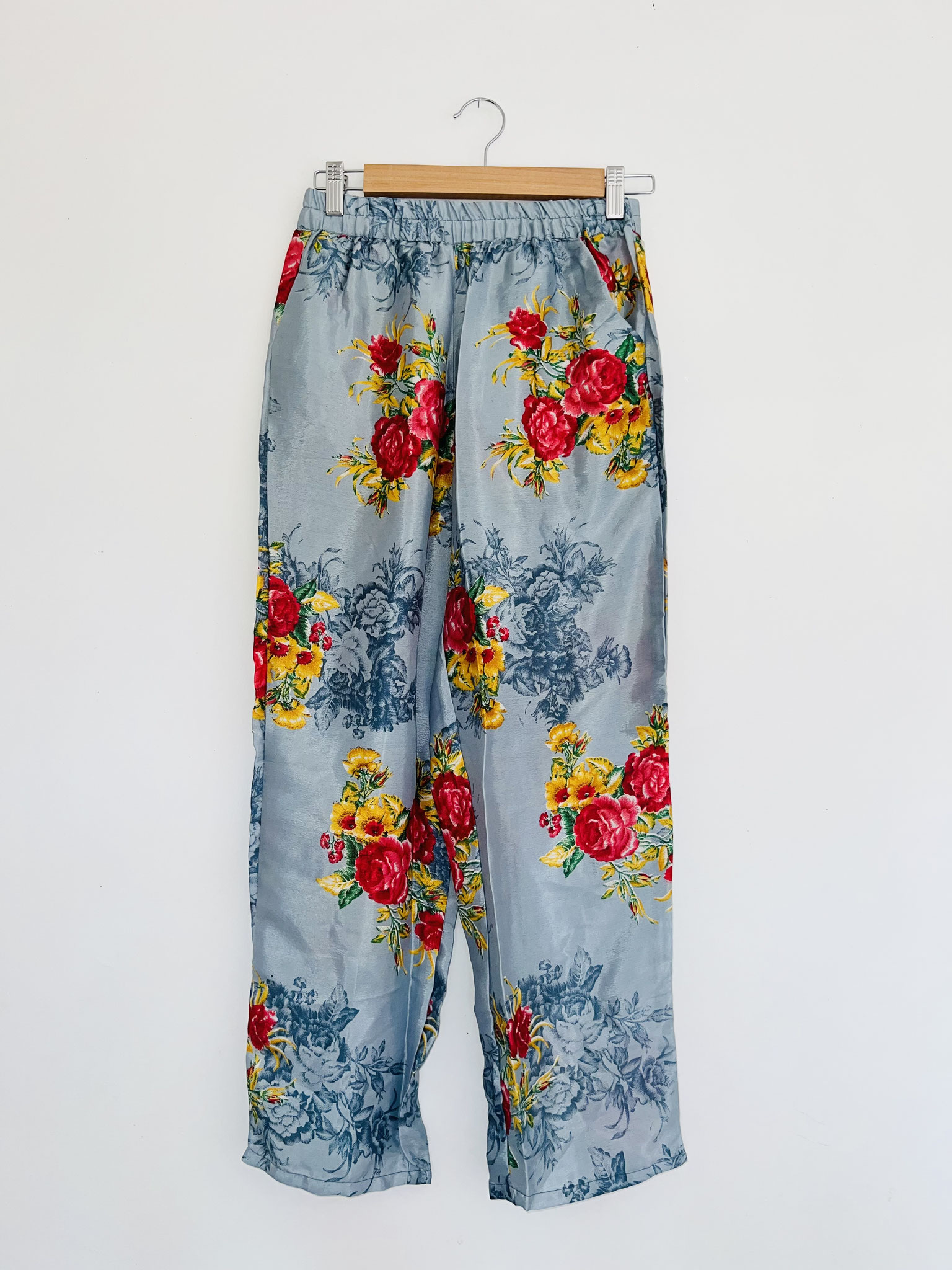 Pantalon gris souris en sari recyclé avec grosses fleurs rouges et jaunes et motifs indiens suspendu sur cintre, vue complète de loin