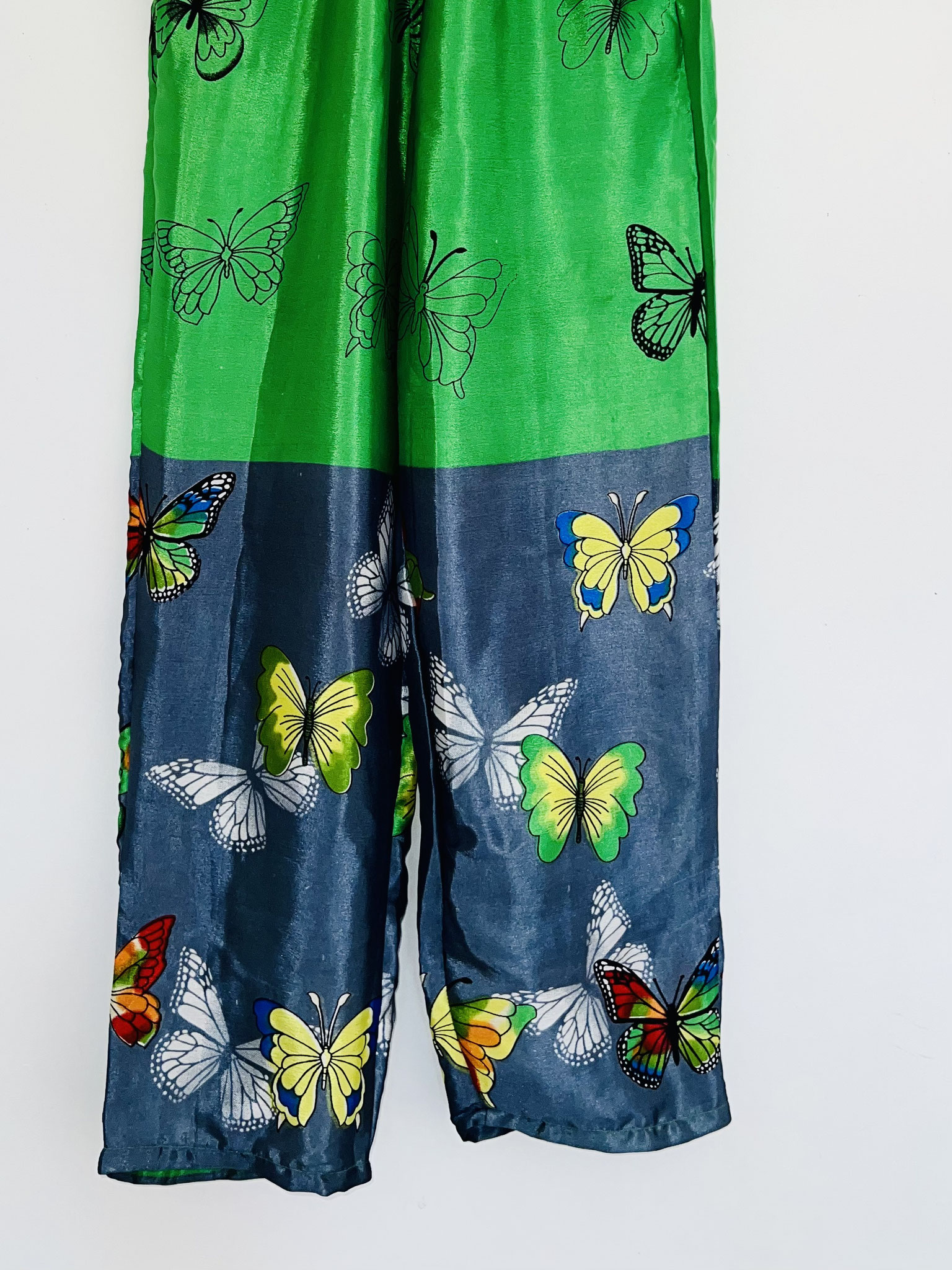 Gros plan sur le bas du pantalon vert vif et gris souris en sari recyclé avec papillons colorés suspendu sur cintre