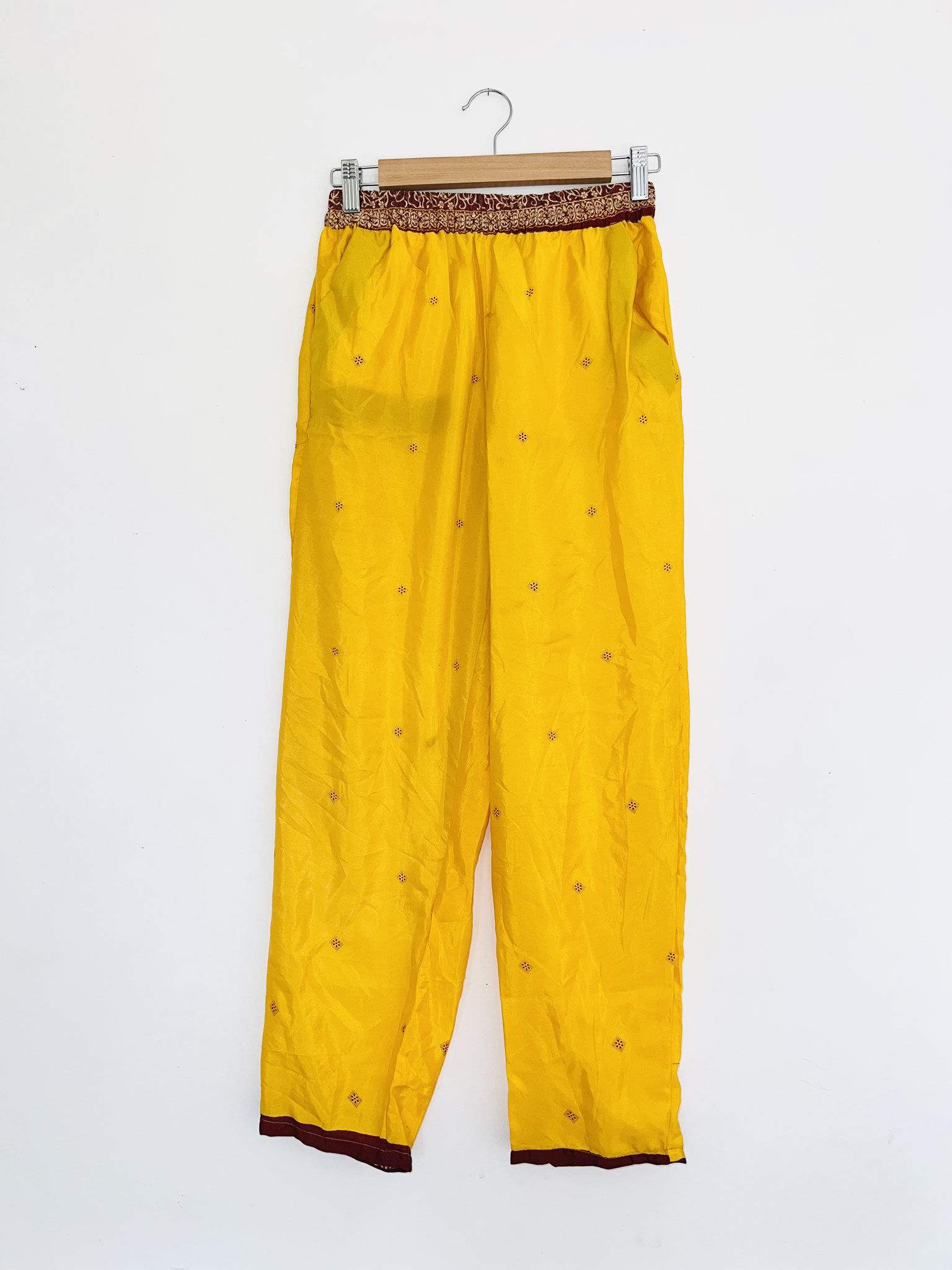 Présenté sur cintre dans son ensemble, ce pantalon bohème en sari recyclé laisse apparaître sa coupe fluide et élégante. Sa ceinture bordeaux souligne la taille et complète parfaitement les motifs indiens du tissu. Une pièce légère et confortable, idéale 