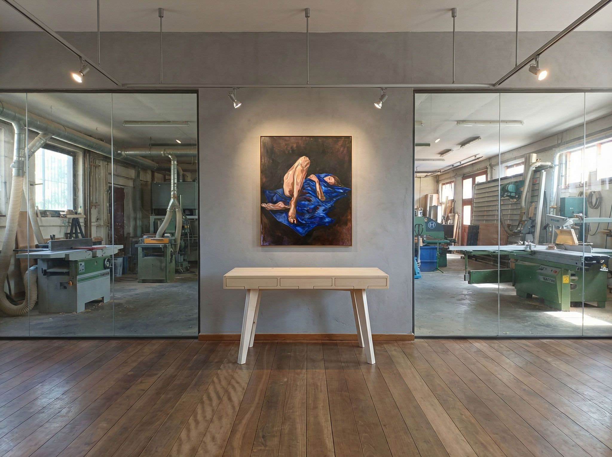 Ein moderner Schreibtisch in hellem Ahorn mit abgeschrägten Beinen im Showroom der Schreinerei Kramhöller mit Blick in die Werkstatt. An der Wand hängt ein Bild von leakramhoeller.com.