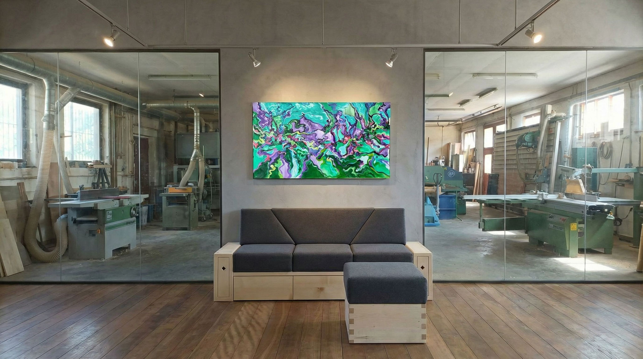 Ein Sofa mit Holzkorpus aus hellem Ahorn mit Schubläden seitlich und unten im Showroom der Schreinerei Kramhöller mit Blick in die Werkstatt. An der Wand hängt ein Bild von leakramhoeller.com.