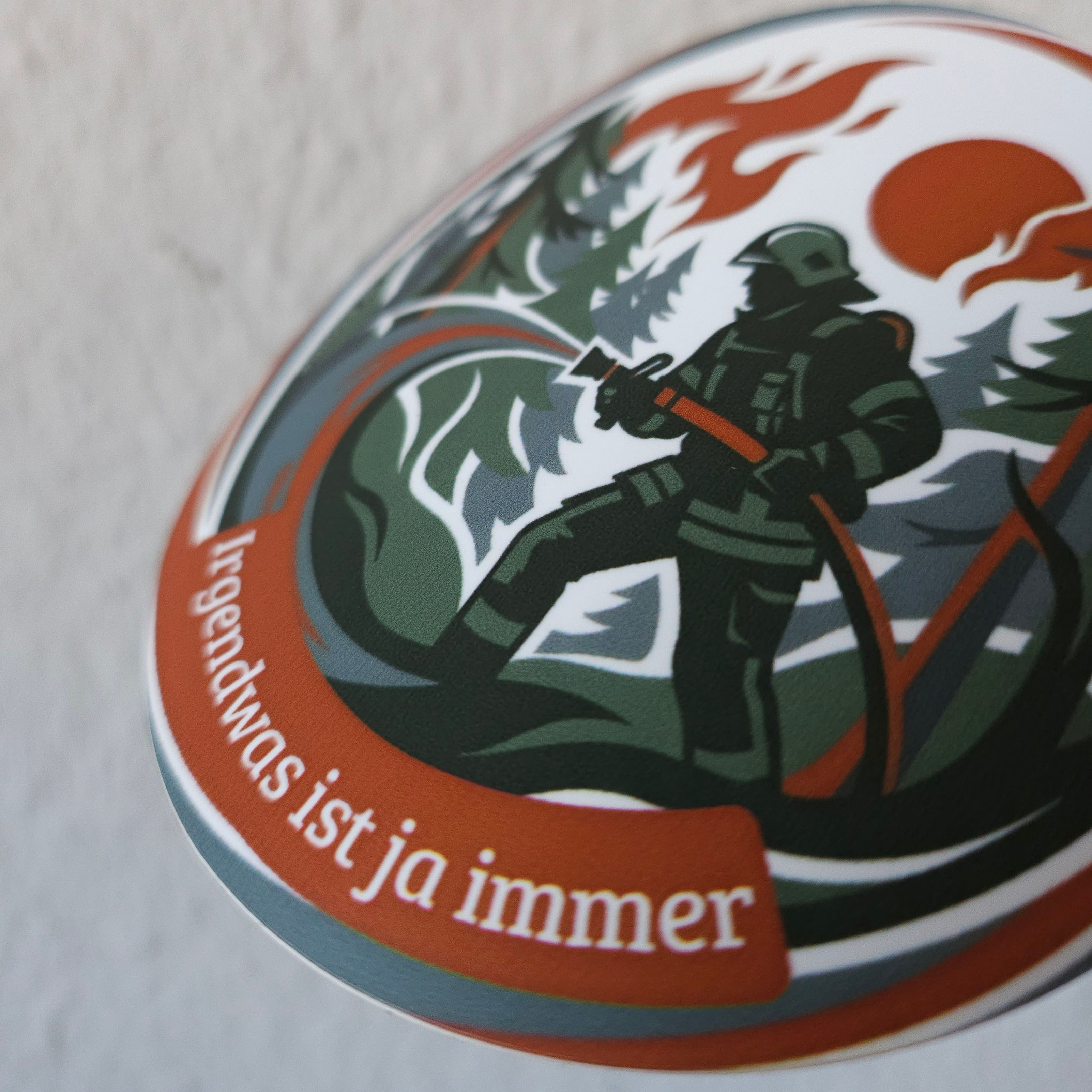 Runder Feuerwehr-Sticker der Einsatzserie zeigt eine Einsatzkraft mit Löschschlauch bei einem Waldbrand im Forst.