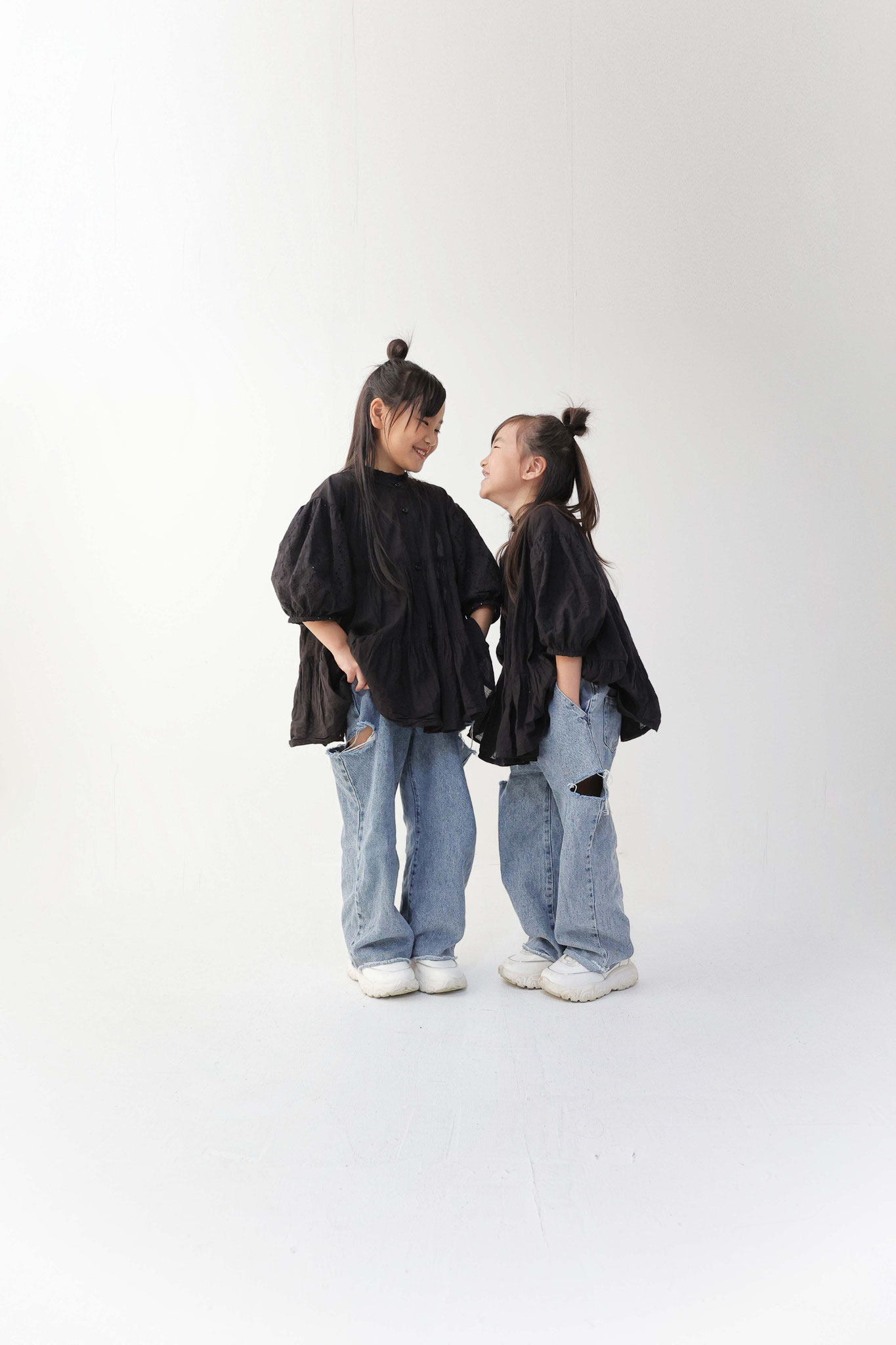 キッズフォト、姉妹での写真白の背景に黒のトップス下はデニムのお揃いコーデ二人で見つめ合い仲睦まじいお写真