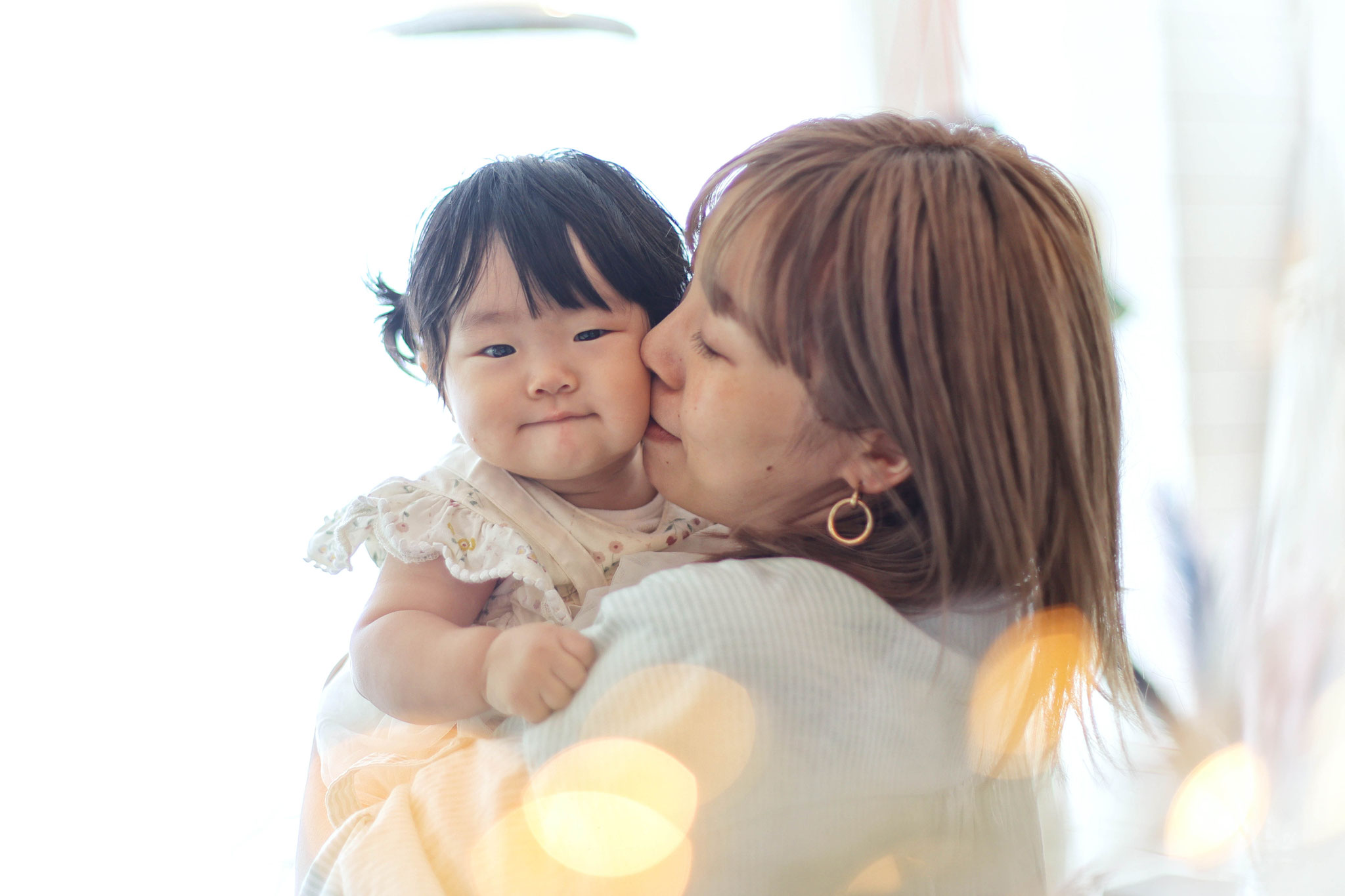 １歳の女の子自然光の中ママに抱っこされてほっぺにチュー！愛らしい素敵な写真
