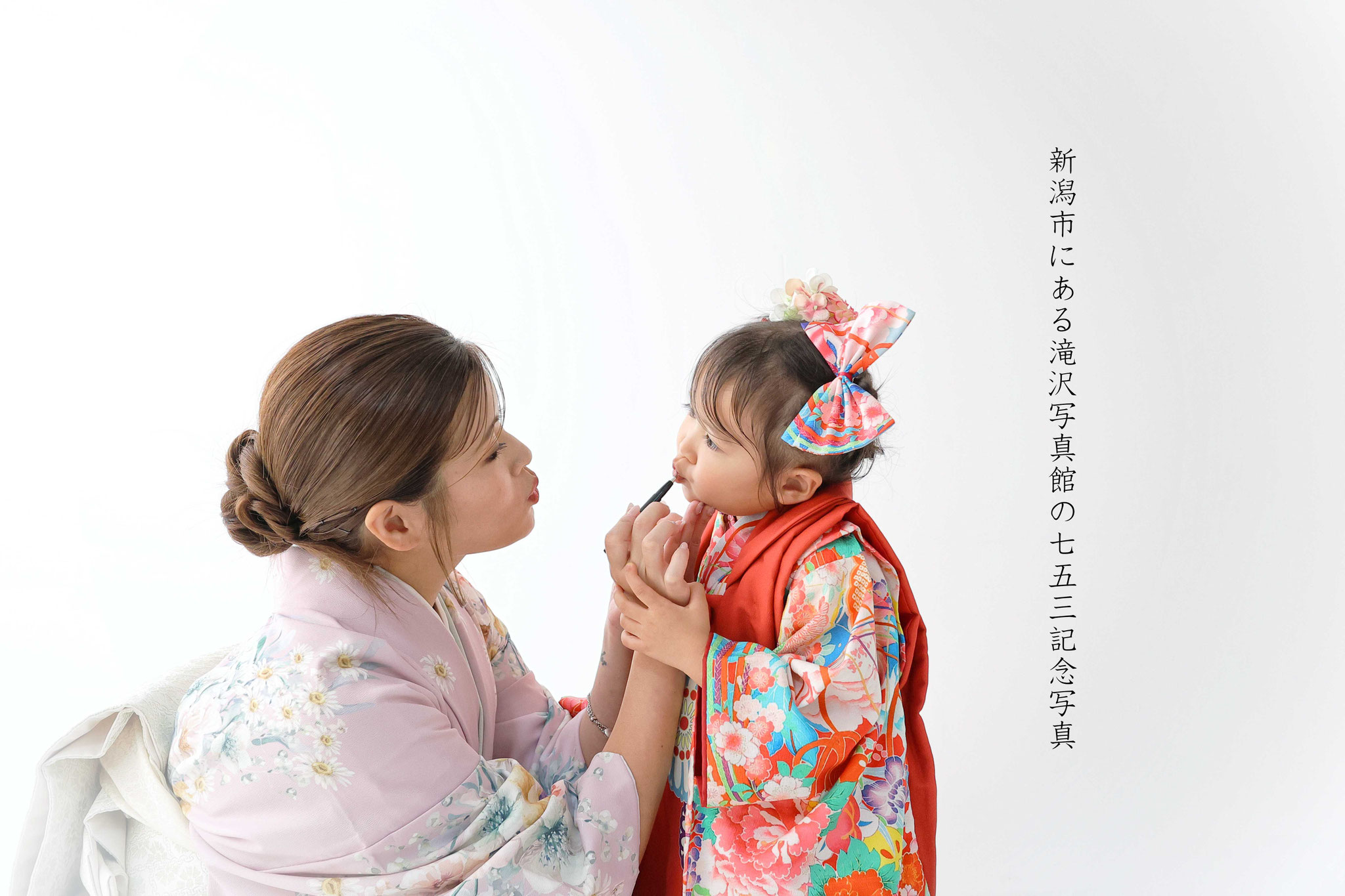 女の子の七五三スタジオの白い背景の前でママに口紅塗ってもらうシーン唇うーてして愛らしい写真