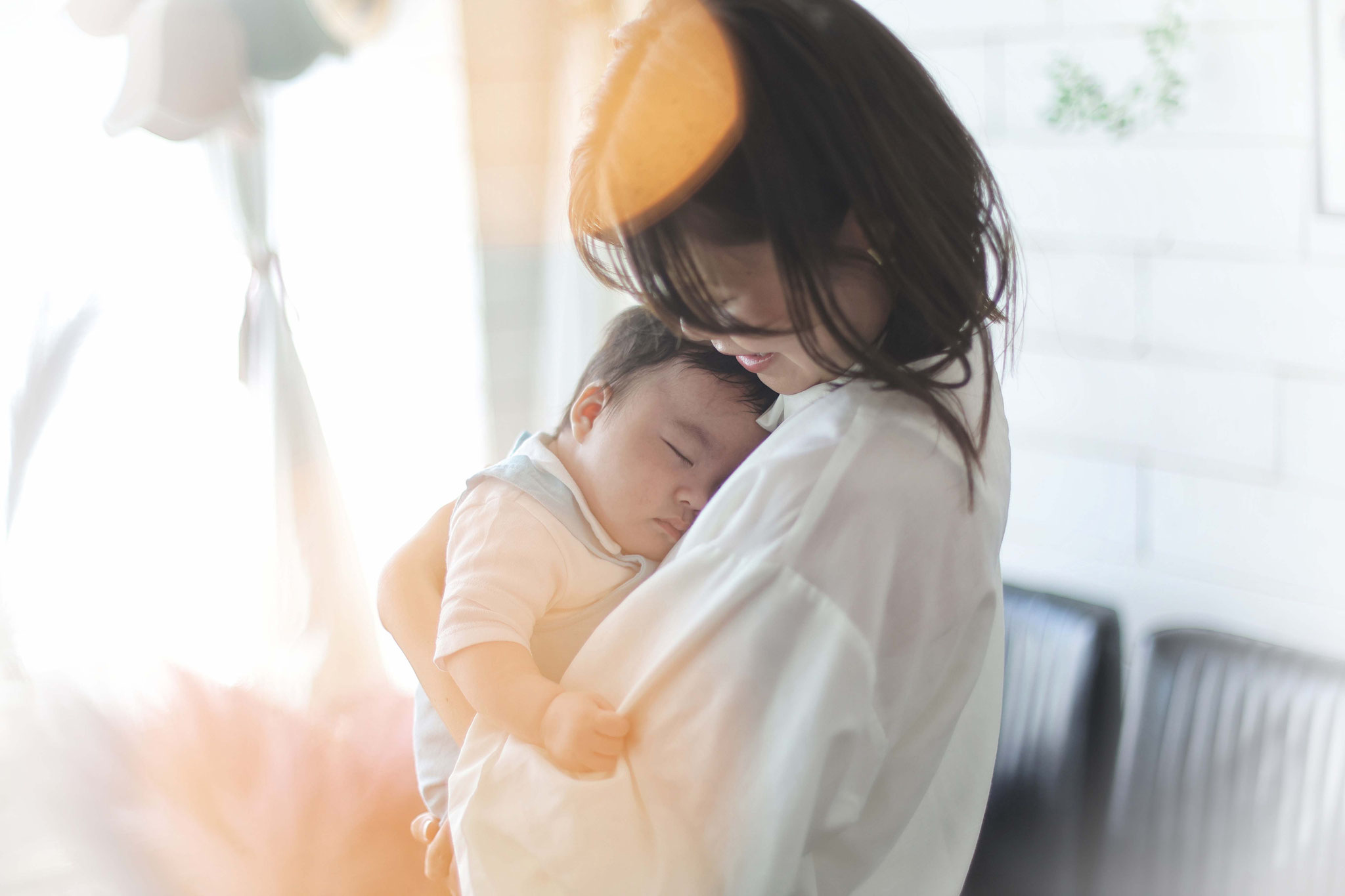 ママに抱かれながら眠る赤ちゃんそれを愛おしく見守るママ素敵な自然光の中で