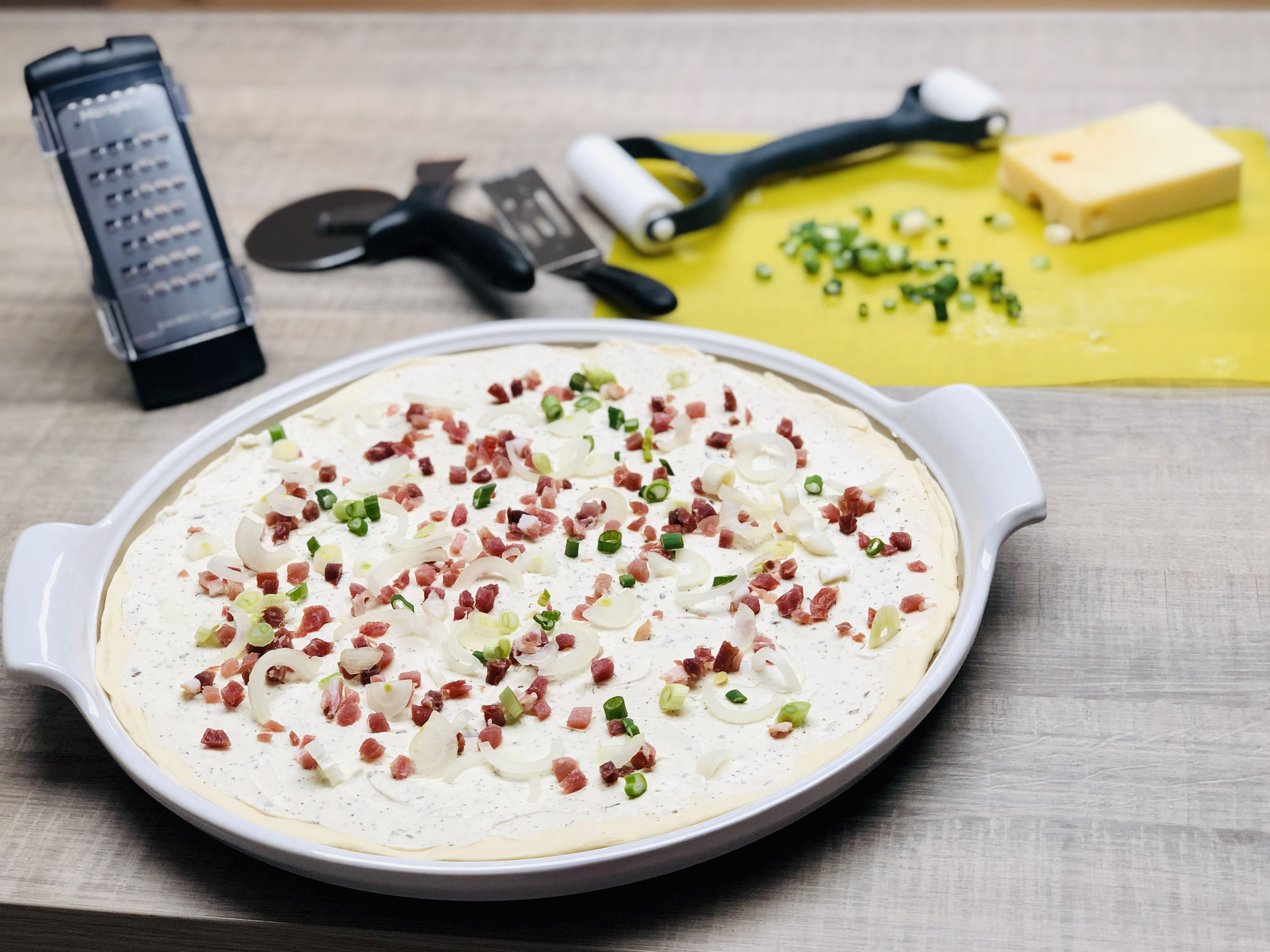 Nun darfst du ganz kreativ deinen Flammkuchen mit Speck, Zwiebeln und Käse belegen