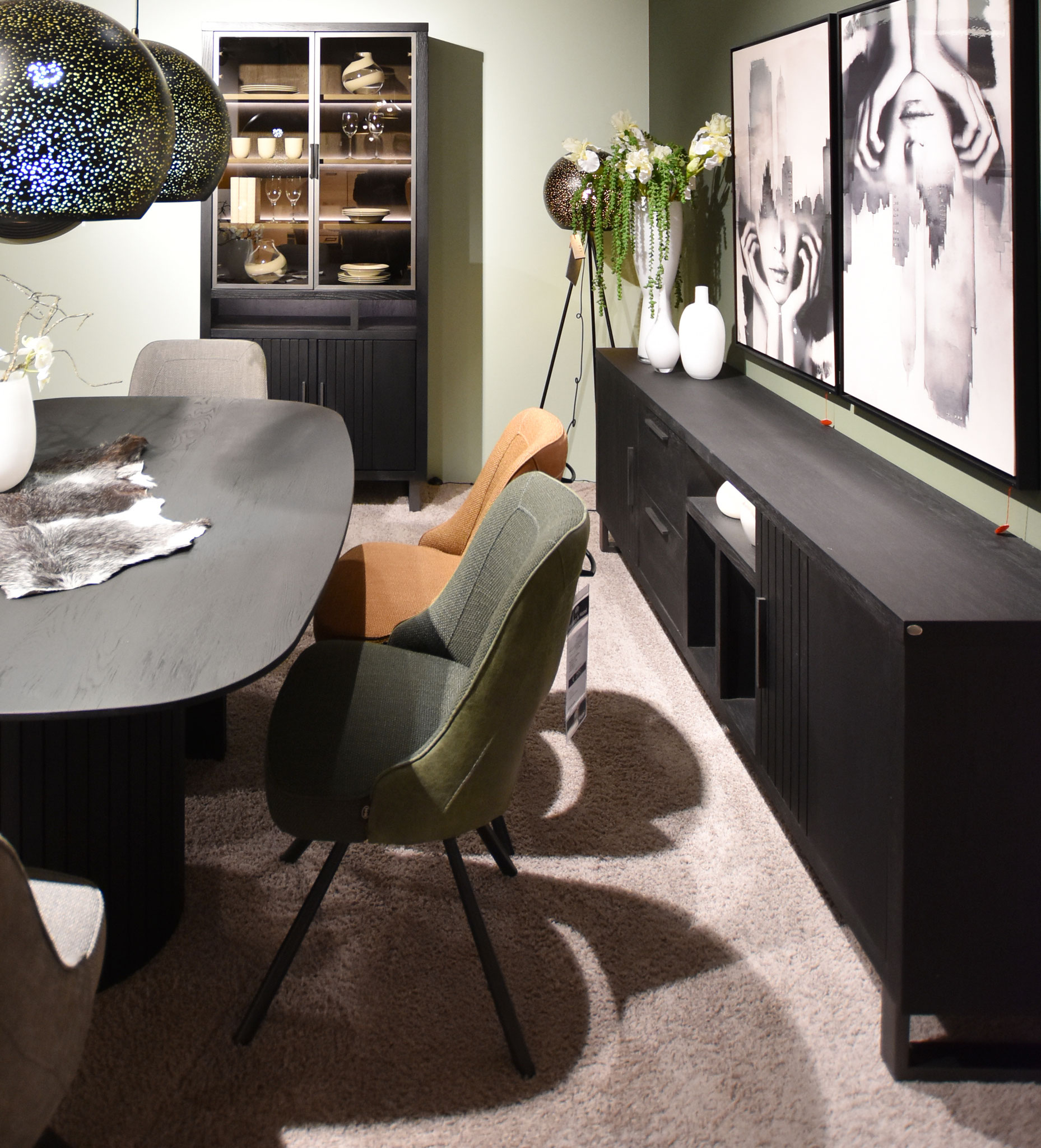 Dunkles Esszimmer mit ovalem, schwarzen Tisch, grünen/orangen Stühlen und Sideboard.