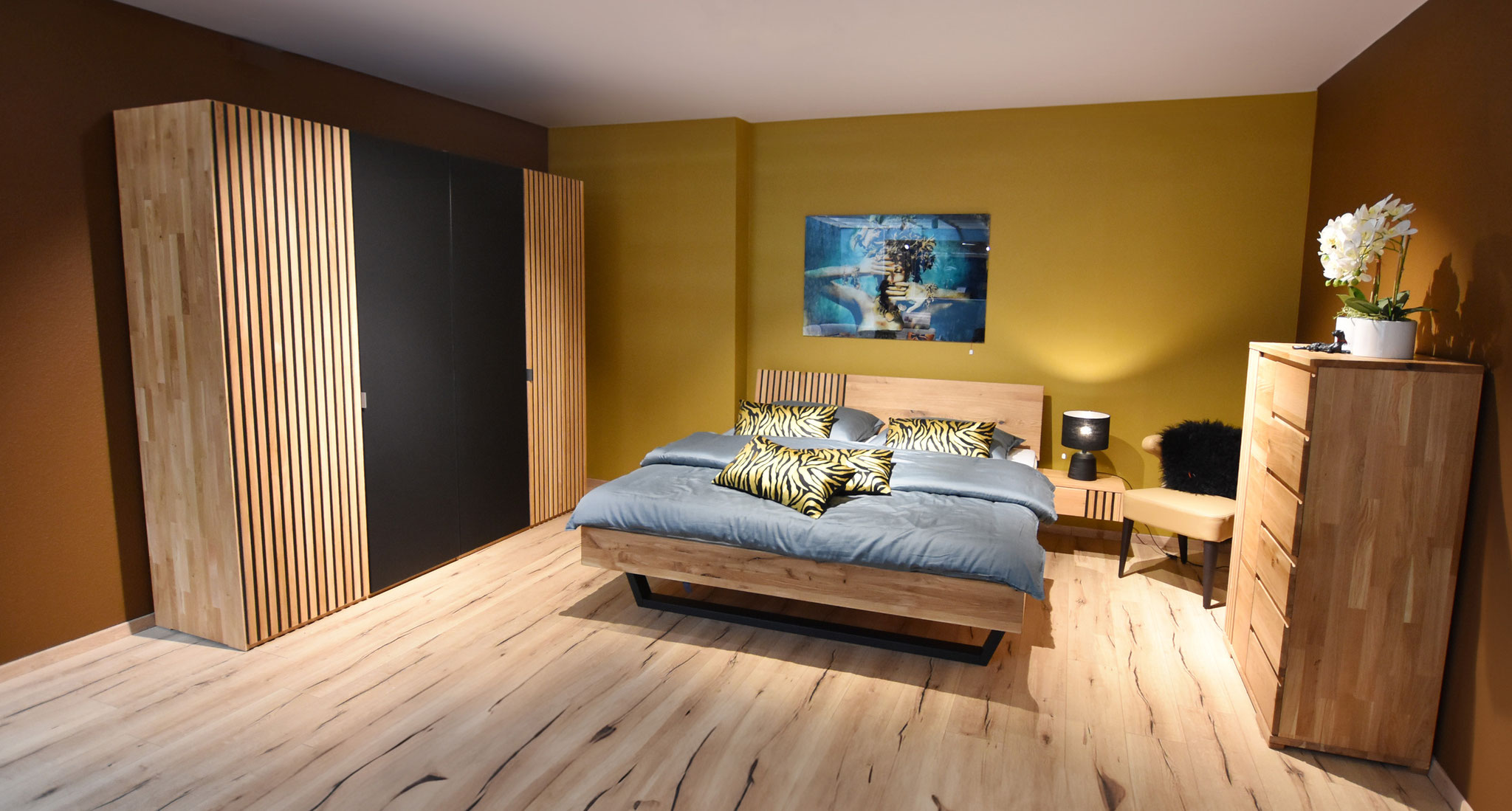 Schlafzimmer mit einem Bett und einem Schrank aus Holz vor einer senfgelben Wand.