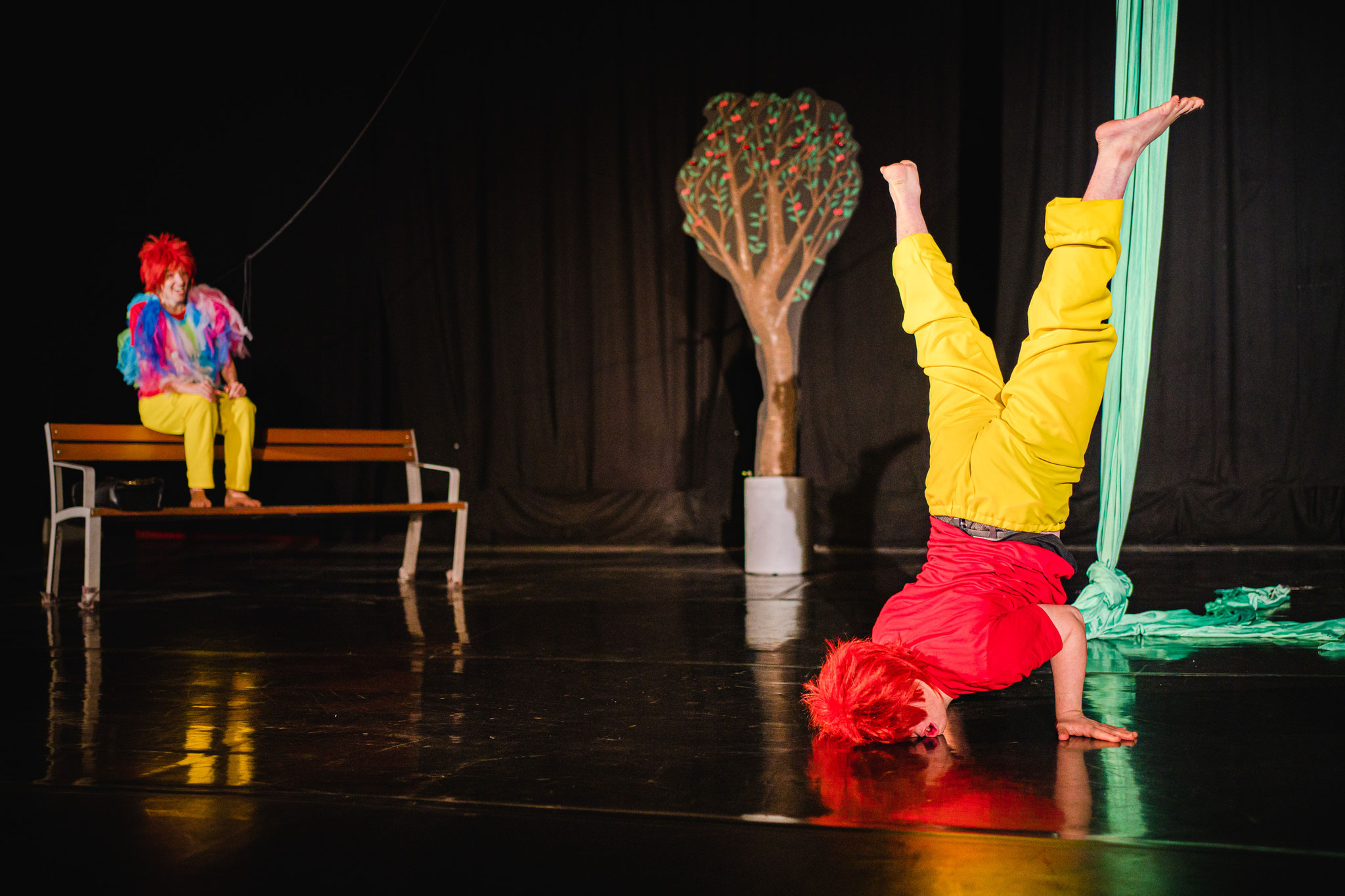 ein Tänzer steht kopfüber und eine Schauspielerin sitzt auf einer Bank u beobachtet ihn