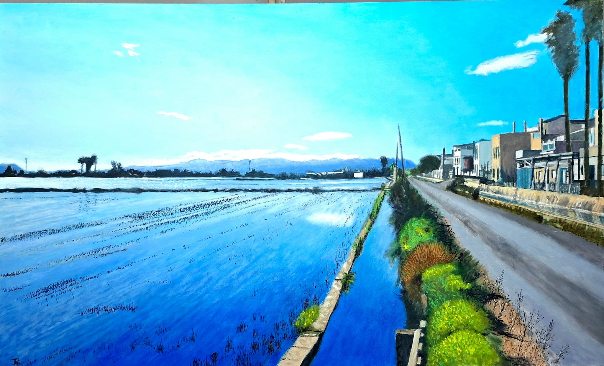 Vista de los arrozales inundados junto al pueblo de El Palmar, con reflejos del cielo y las montañas al fondo; a la derecha, las casas y palmeras que marcan la frontera entre el paisaje natural y la zona urbana.