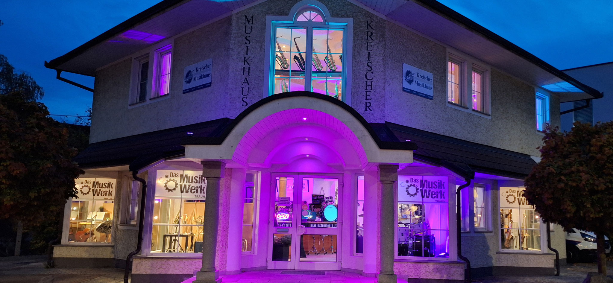 Außenansicht des MusikWerk Traun bei Nacht mit beleuchtetem Schaufenster und Instrumentenausstellung.