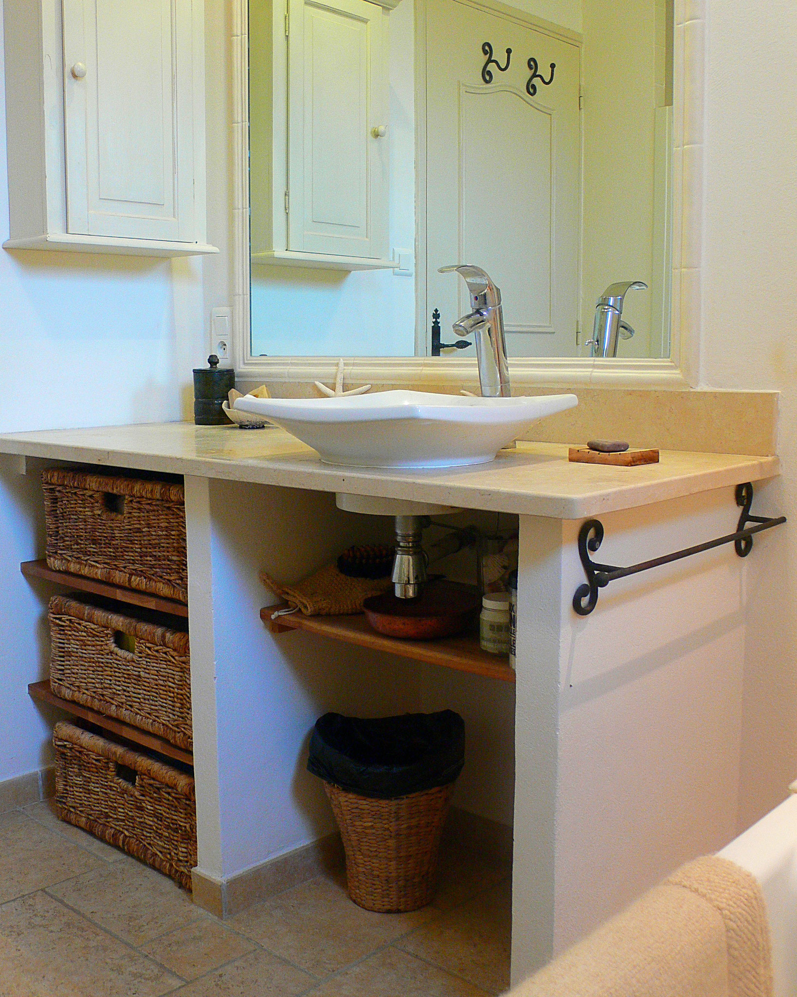 Salle de bain intemporelle en blanc et beige. Meuble vasque maçonné sur mesure avec tiroirs en rotin tressé et étagères en chêne, plan en pierre naturelle vieillie.