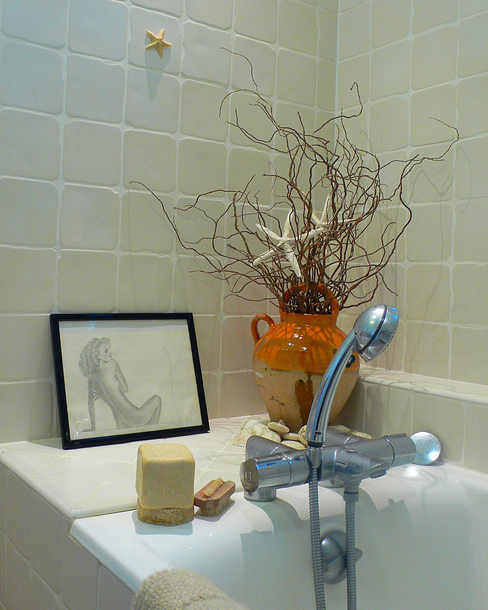 Salle de bain intemporelle en beige et blanc. Détail jarre ancienne vernissée jaune avec branchages, faïences murales artisanales et croquis de nu personnel.