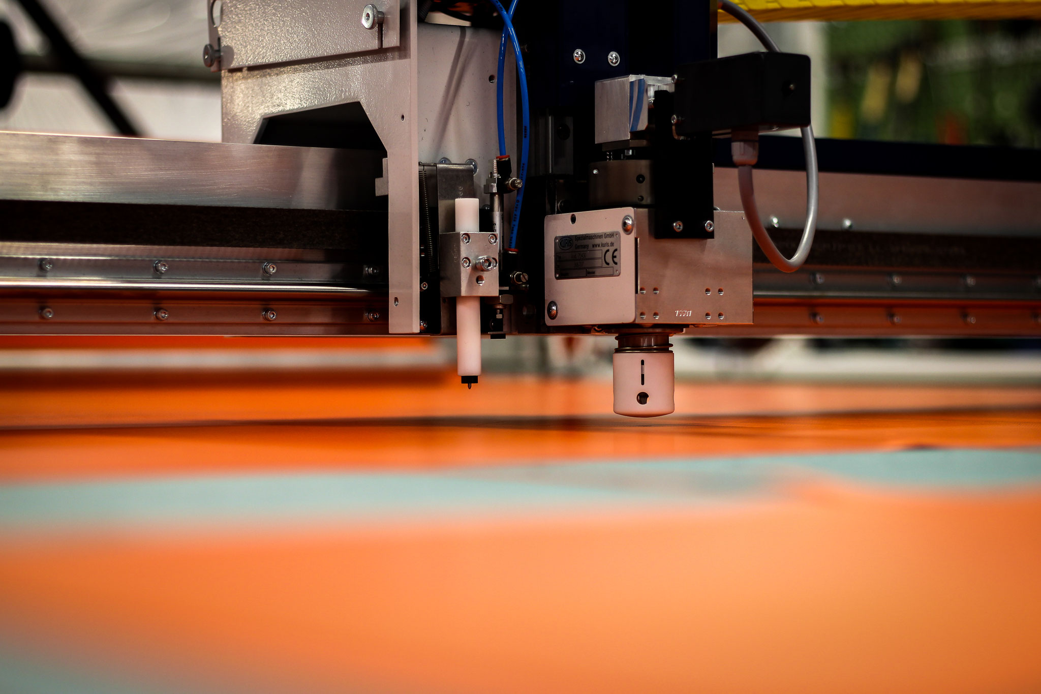 Zu Beginn werden Planenmaterial und Baumwollstoff zugeschnitten. Die Rolle mit dem Rohmaterial wickelt sich hierbei automatisch ab, während ein Messer die zuvor programmierten Wege abläuft