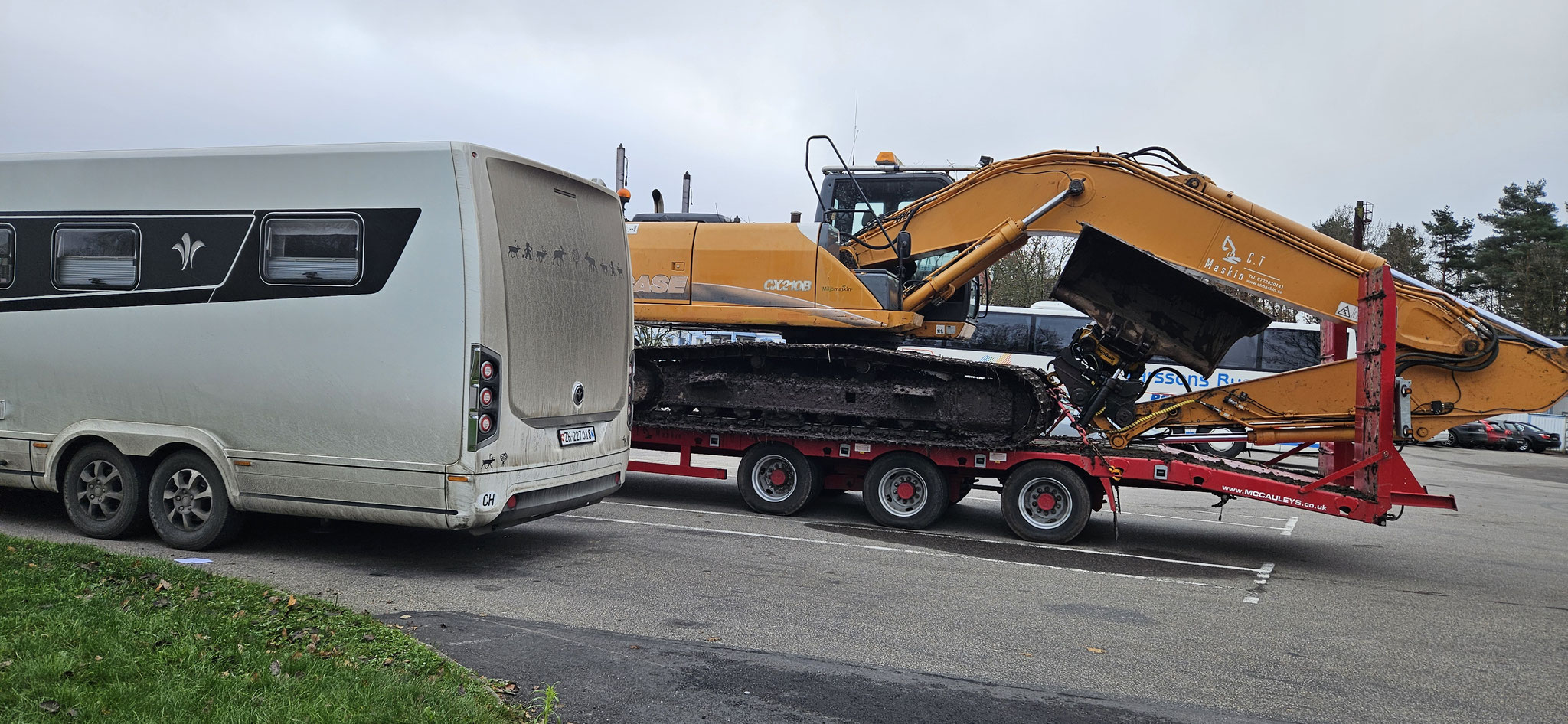Was macht der Traktor mit Raupenbagger-Ladung auf einer Autobahn-Raststätte?