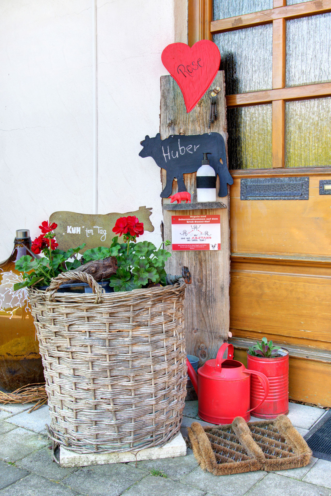 Eingang vom Ferienhaus mit blumenkorb, roten gieskannen und kuhschild