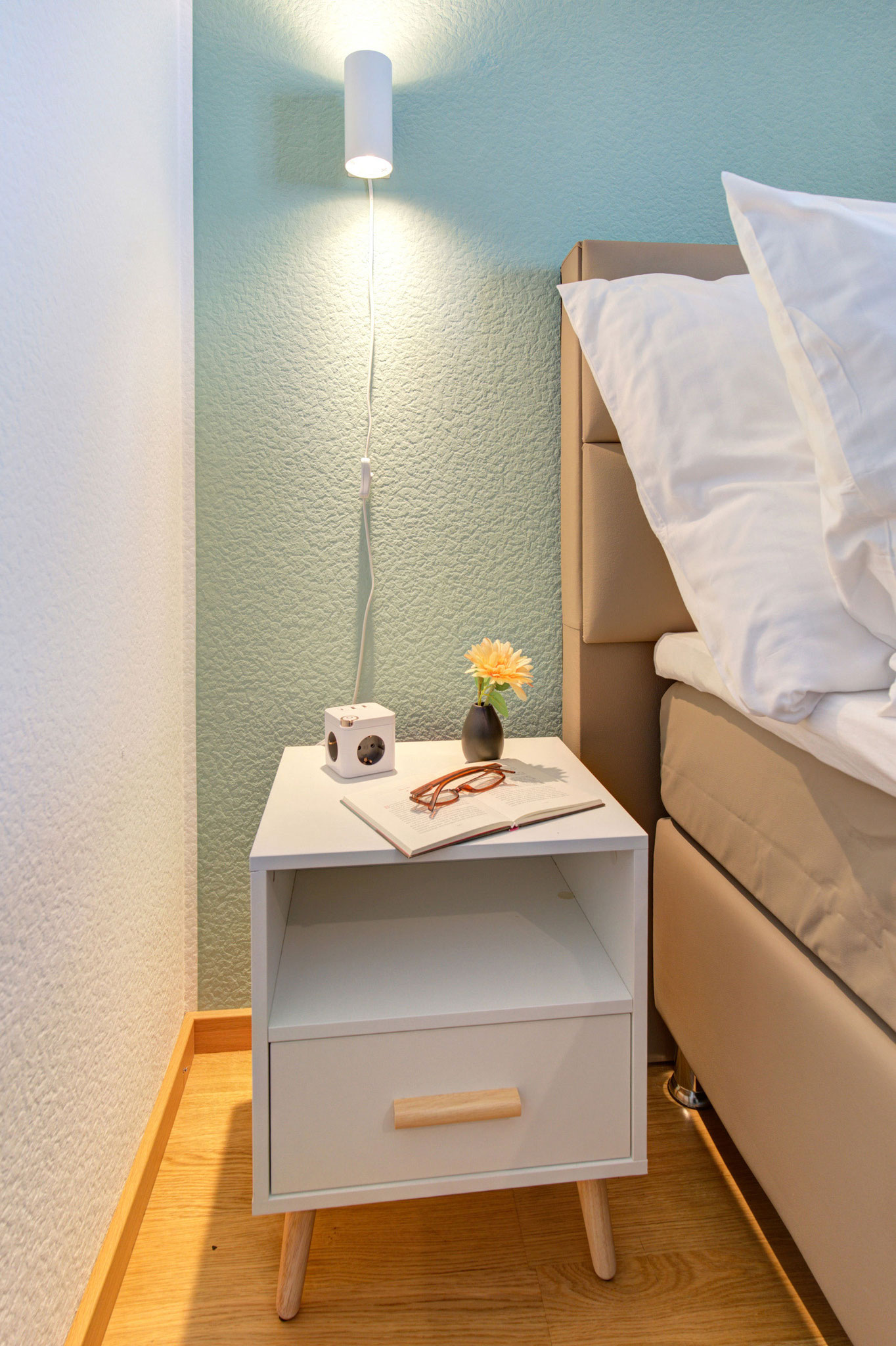 nachttisch mit kleiner schwarzer vase und gerbara sowie usb-würfel ferienwohnung