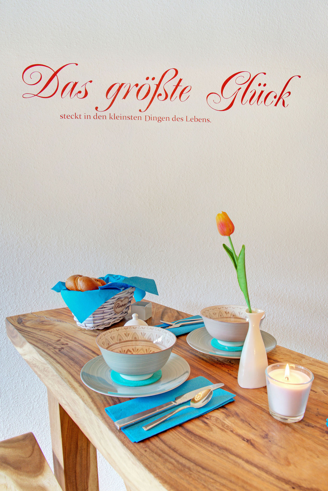 Frühtückstisch für zwei Personen gedeckt in türkis und Beschriftung das große Glück auf wand in ferienwohnung